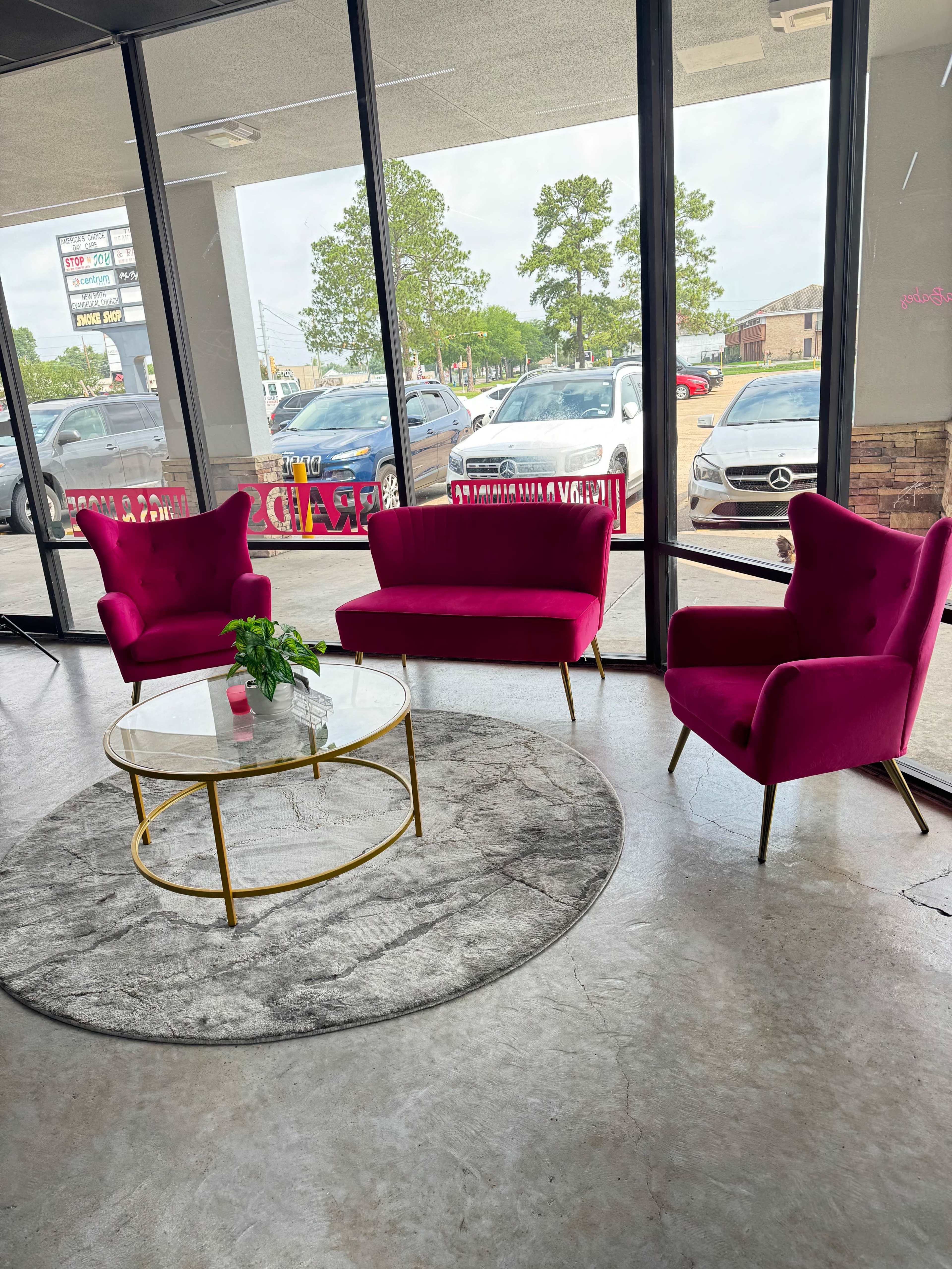 The image shows a modern interior featuring two pink chairs and a matching pink sofa arranged around a round coffee table on a gray circular rug.