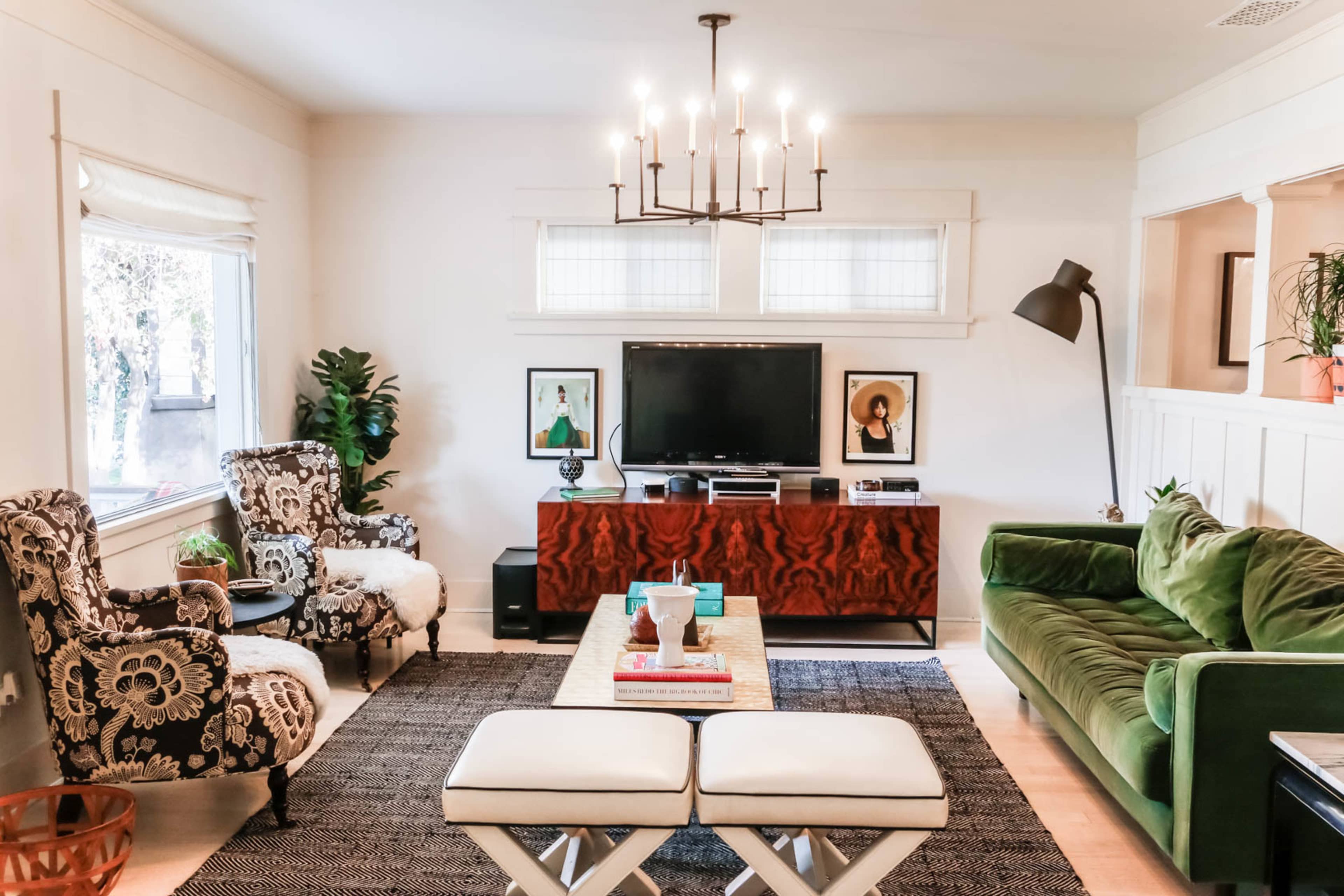 A living room features a green sofa, a wooden media console with a television, two patterned armchairs, and a coffee table on a textured rug.