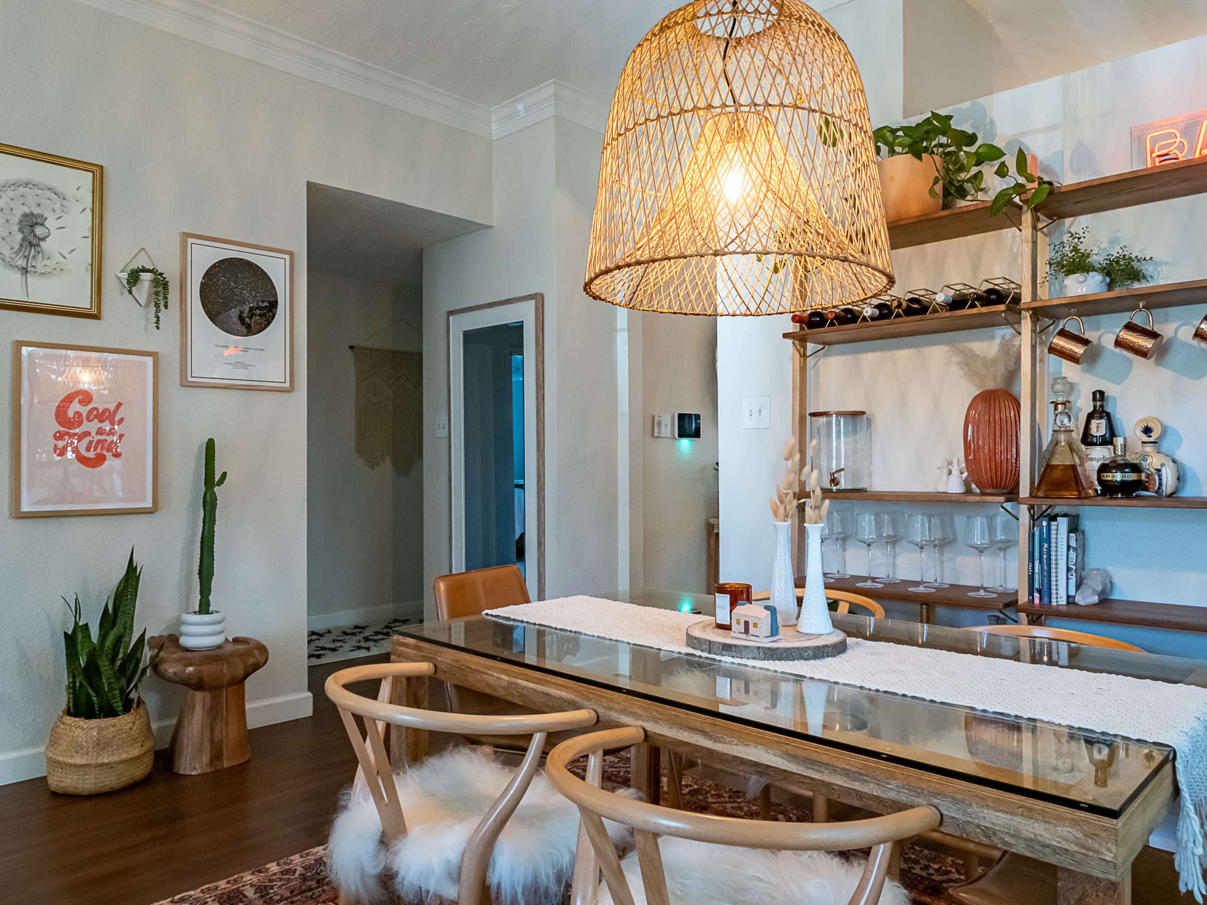 A modern dining area features a wooden dining table with glass top, surrounded by light-colored chairs, and a large woven pendant light hanging above.