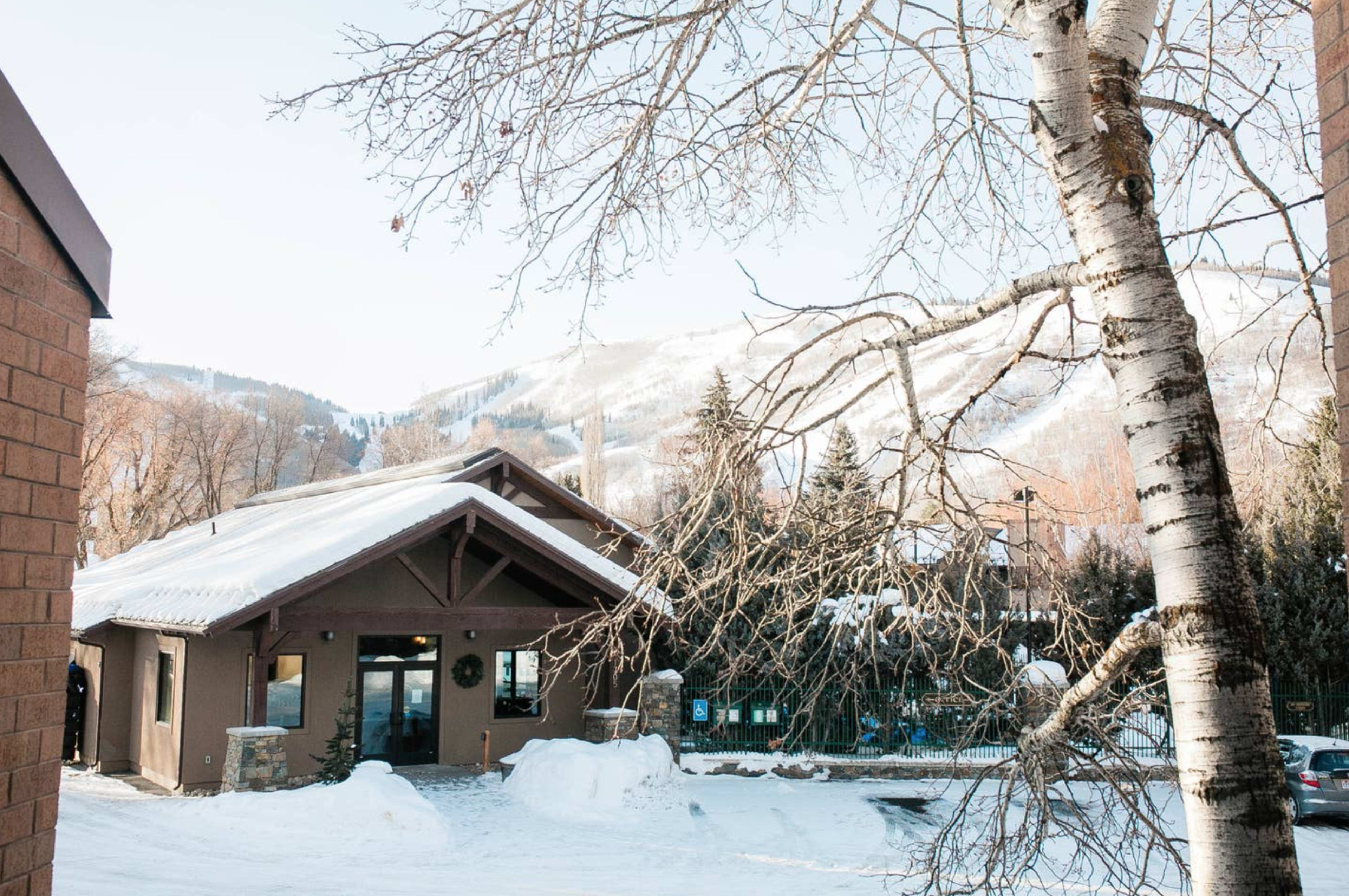 A mountain lodge surrounded by snow-covered ground and bare trees, with a distant view of mountains in the background.