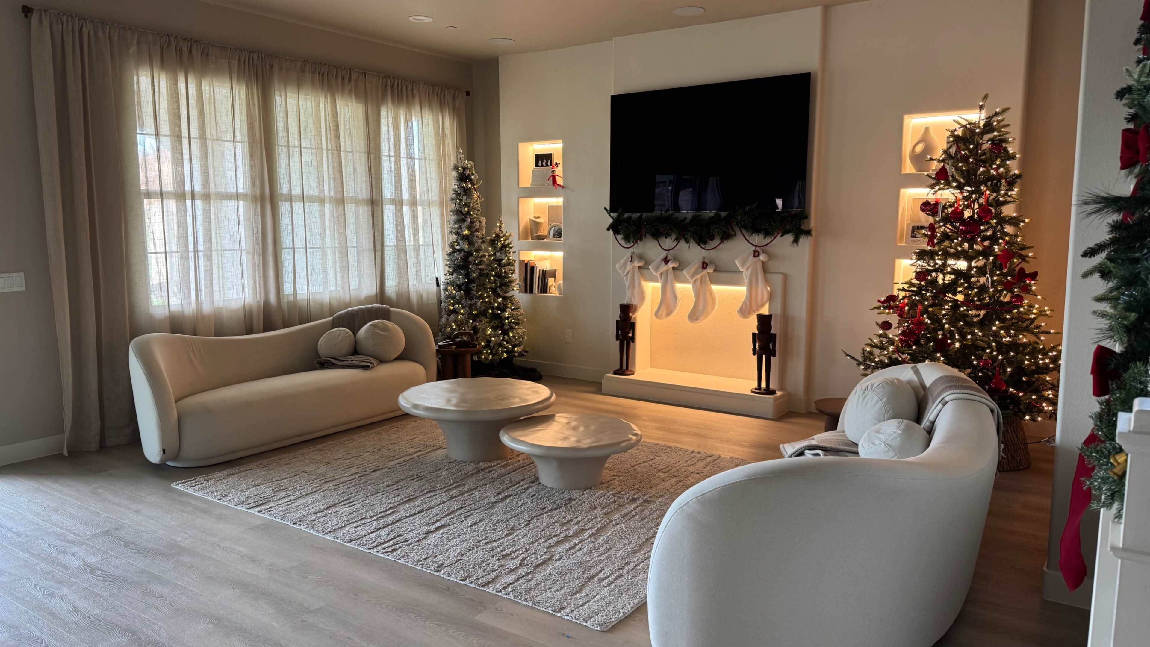 The living room features two curved white sofas, a coffee table, and holiday decorations including two Christmas trees and stockings hung on a fireplace.