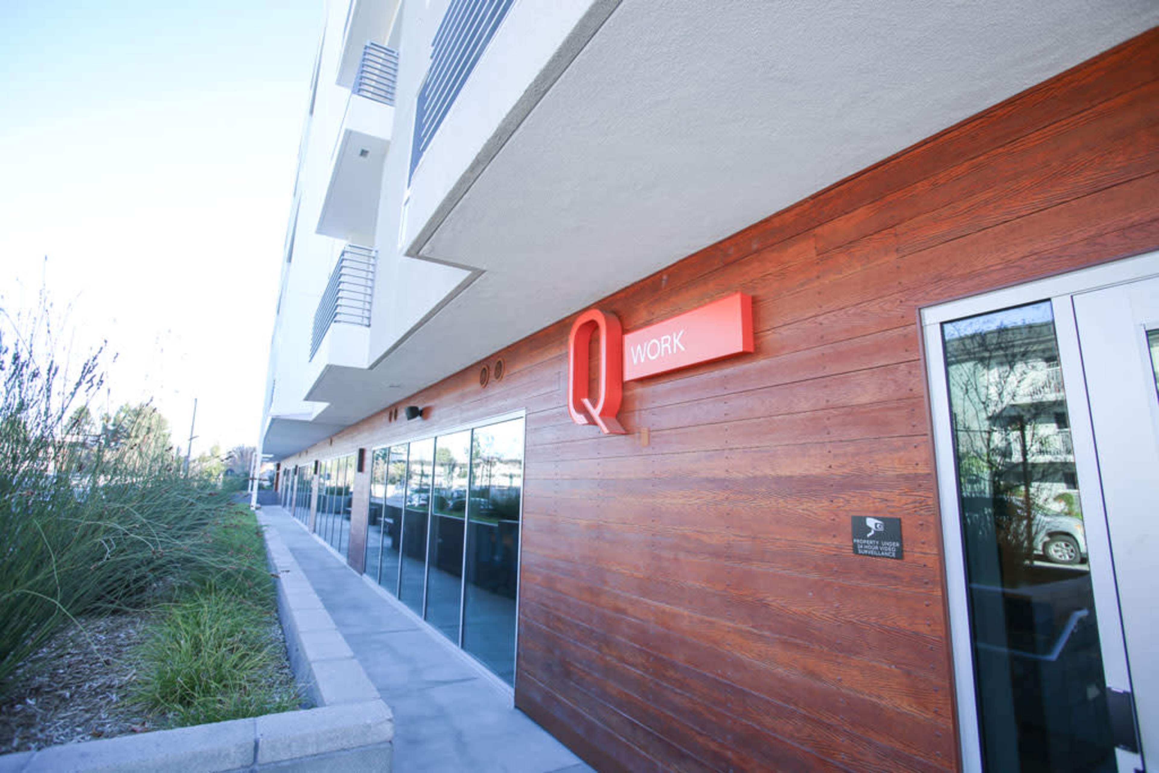 The exterior of a modern building features a wooden facade with a bright red sign that reads "Q WORK."