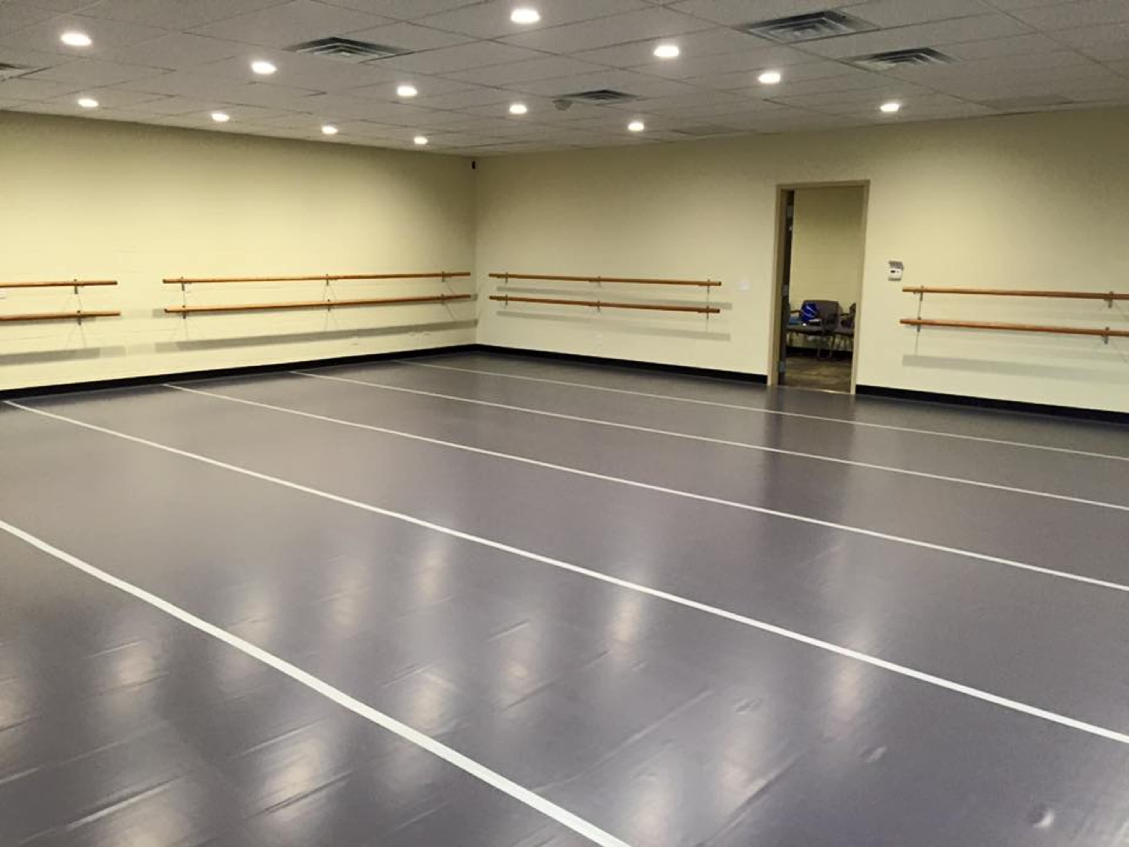 A spacious dance studio with a smooth gray floor and wall-mounted ballet bars.
