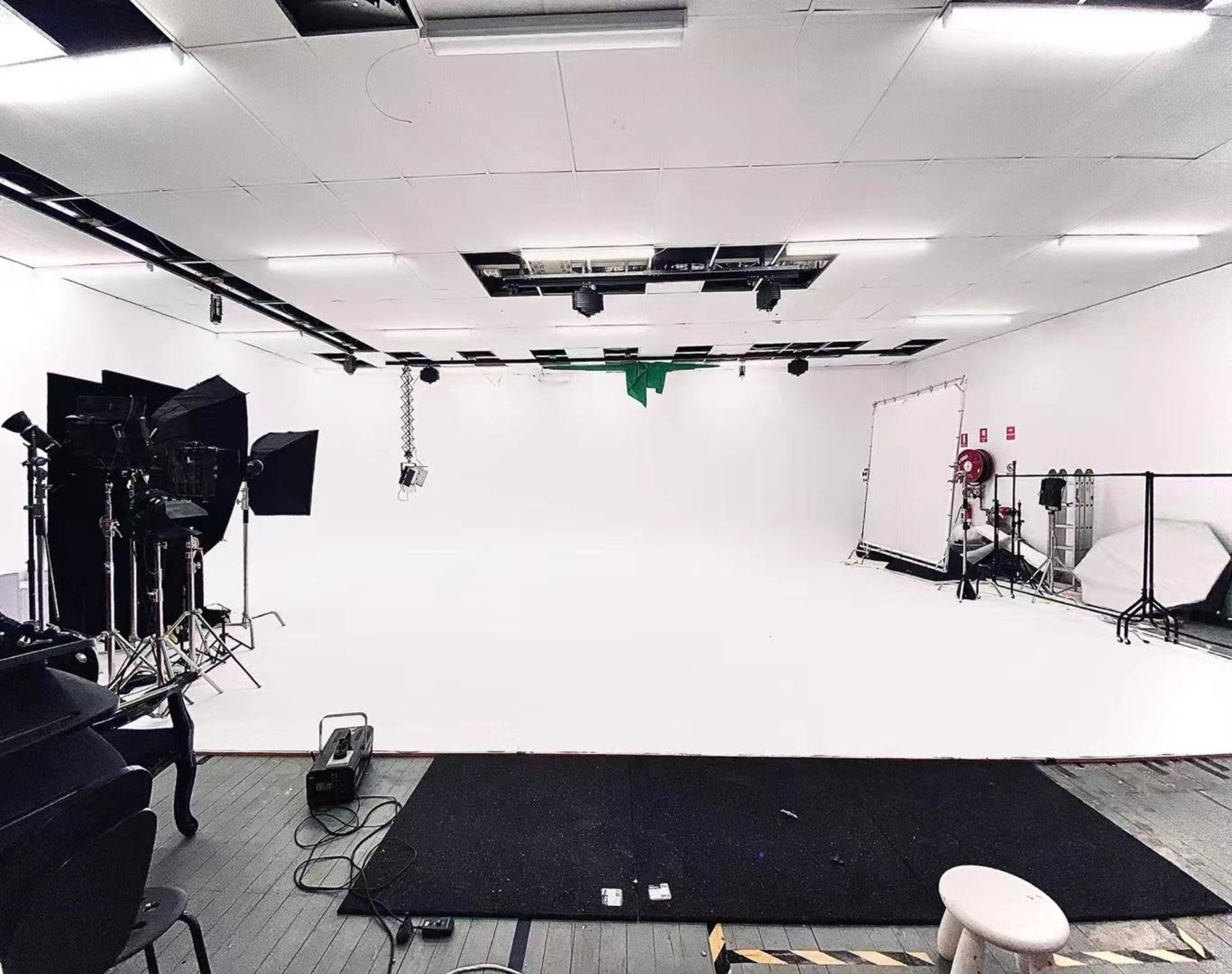 A spacious studio setup with white walls and floor, equipped with lighting equipment and a green screen in the background.