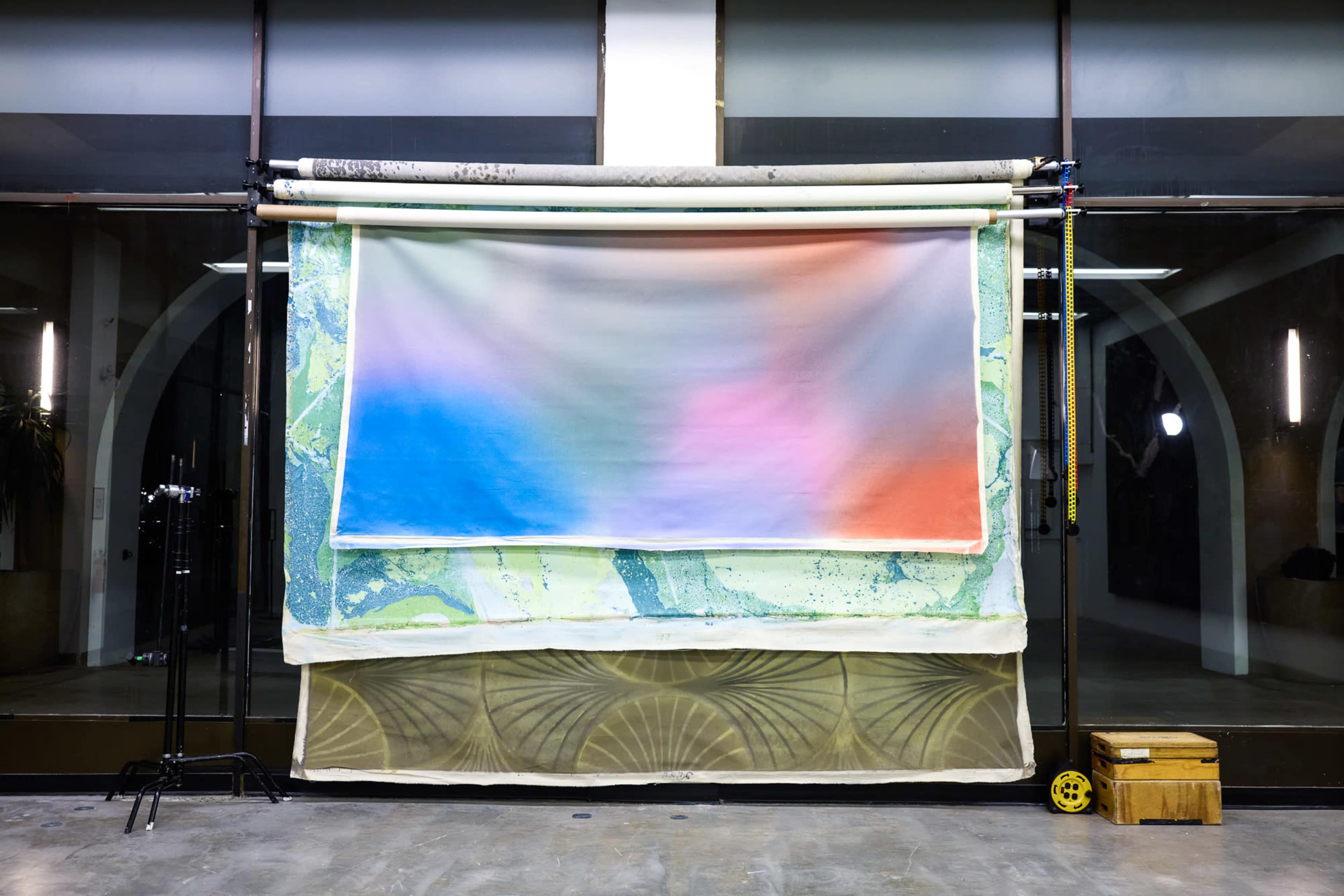 A large backdrop featuring a gradient of colors is set against a minimalist studio space with tall windows.