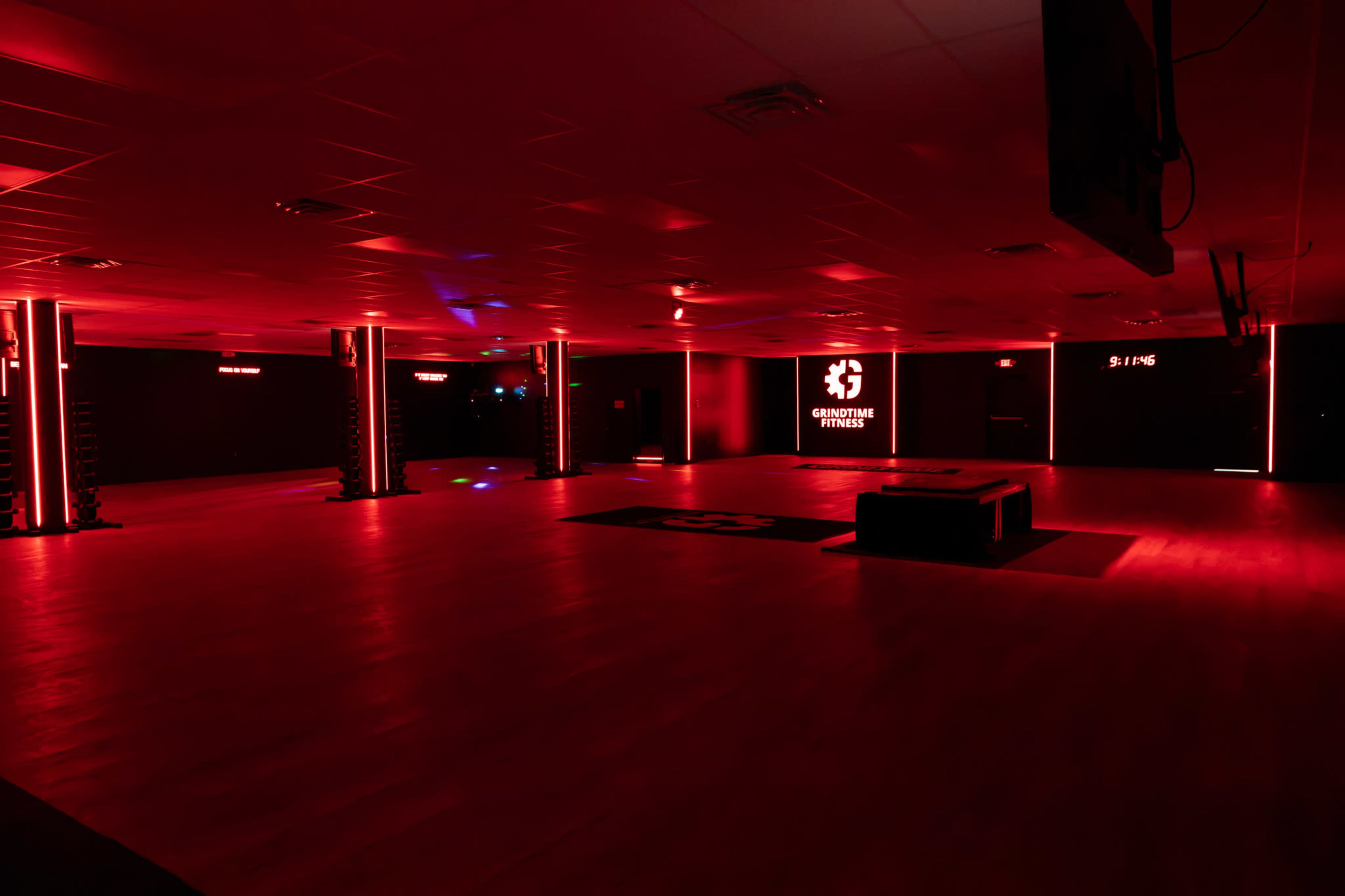 The interior of a fitness studio is lit with red lights, featuring a workout area with a bench and branding on the walls.