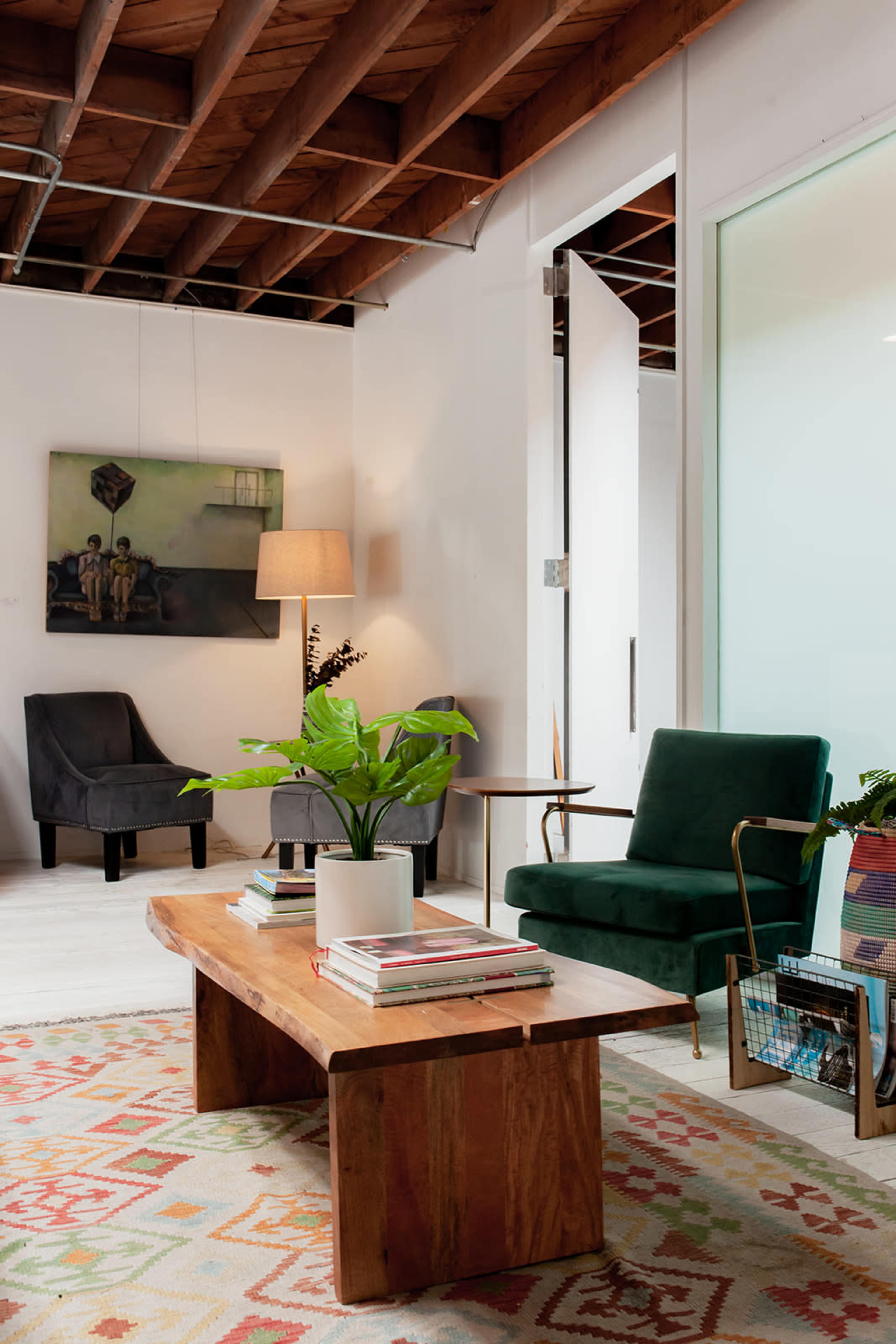 The image shows a modern interior space featuring two armchairs, a wooden coffee table with books, a potted plant, and a lamp beside a wall art piece.