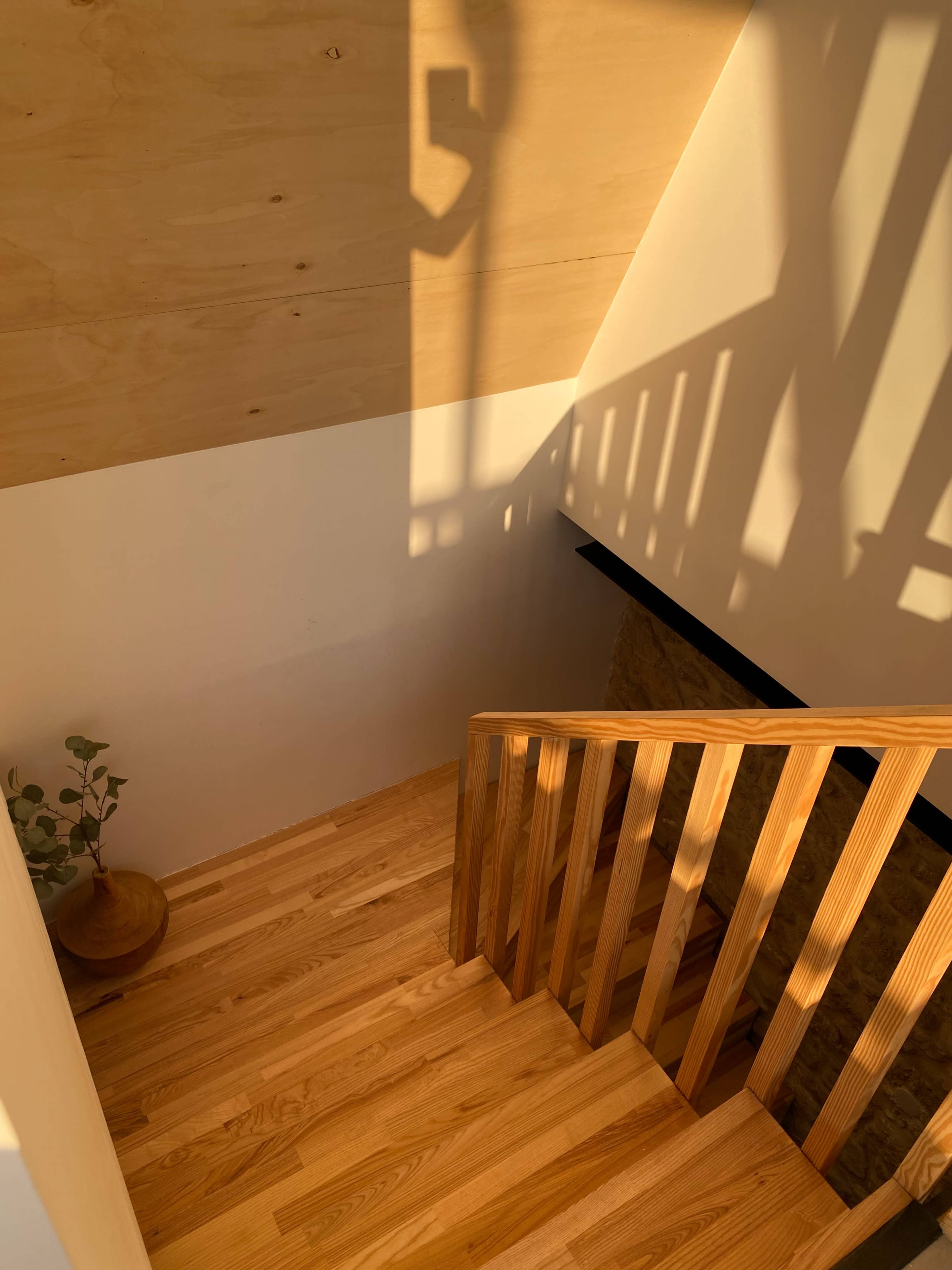 A wooden staircase leads down to a lower level, with sunlight casting shadows on the walls.