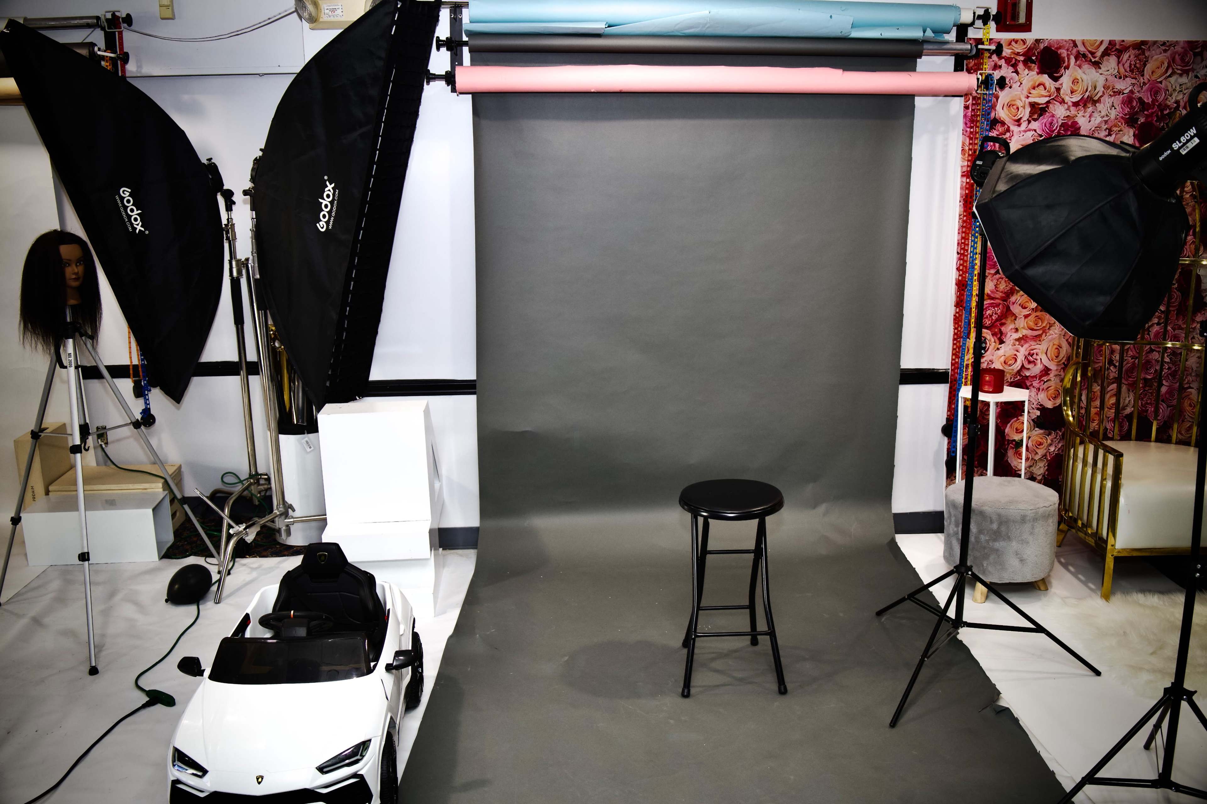 A photography studio setup with a gray backdrop, a black stool, and multiple softbox lights, along with a toy car positioned nearby.