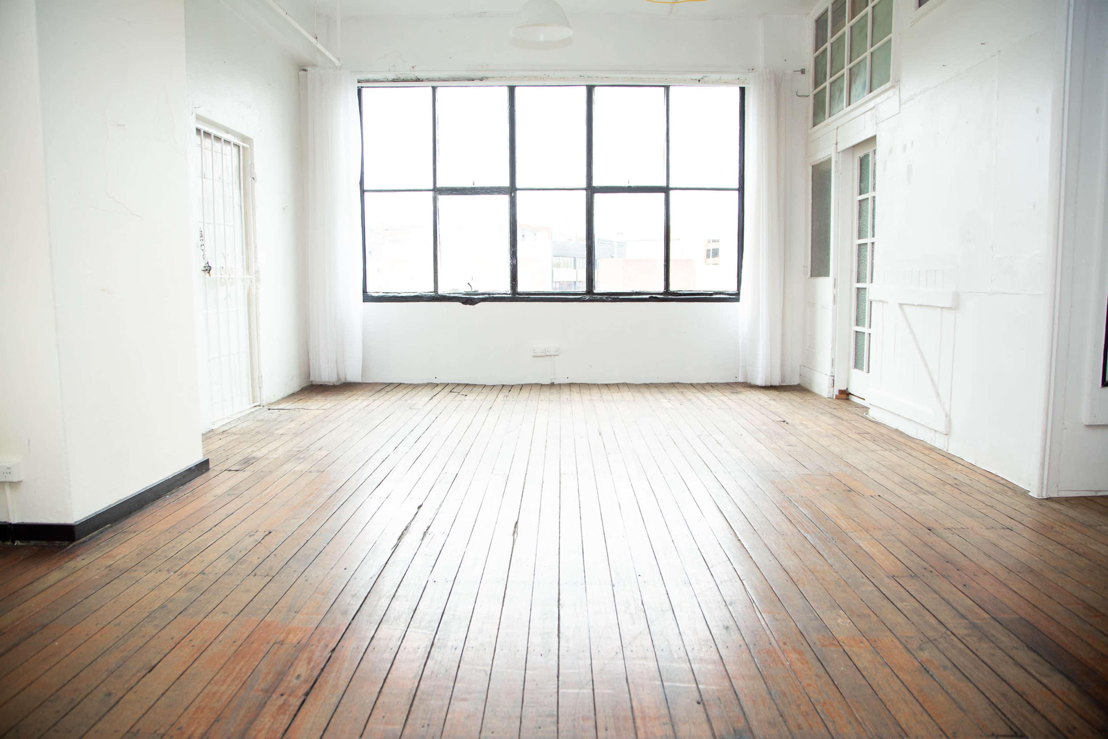 An empty room with wooden floors and large windows allowing natural light to enter.