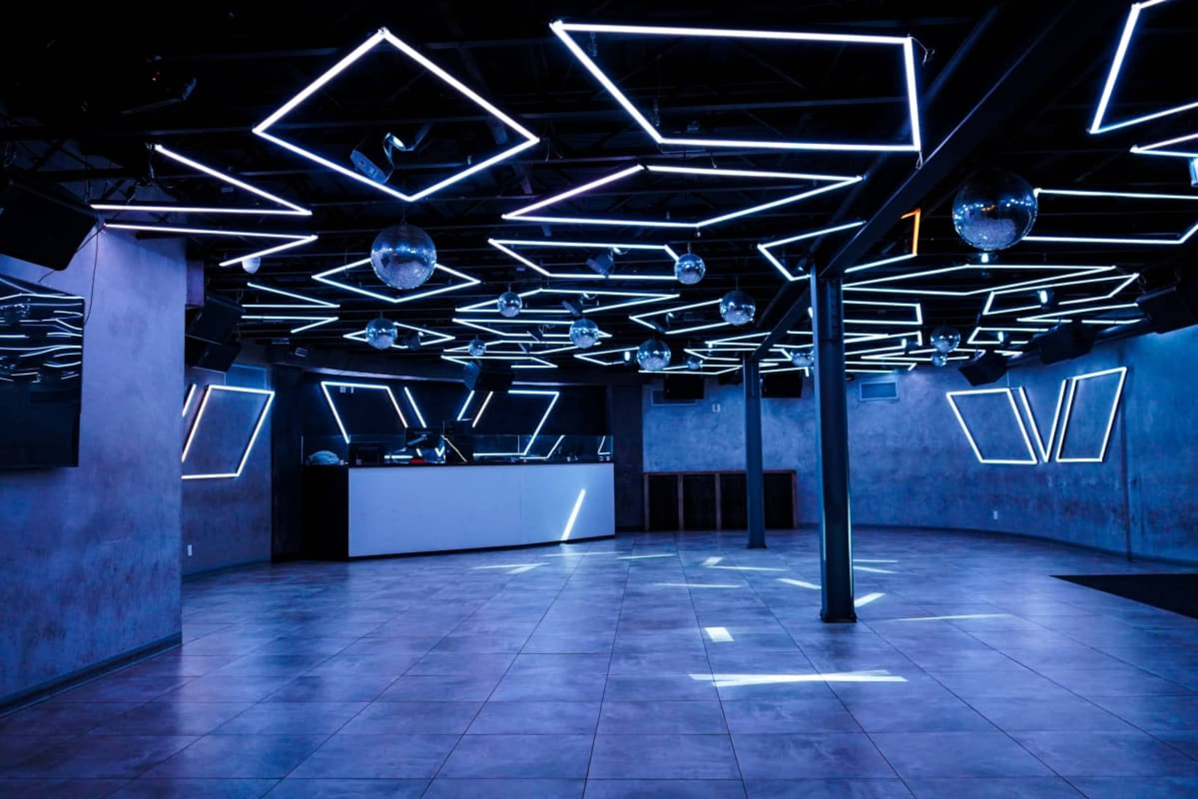 The image shows an empty nightclub with a geometric ceiling design featuring blue LED lights and mirrored disco balls.
