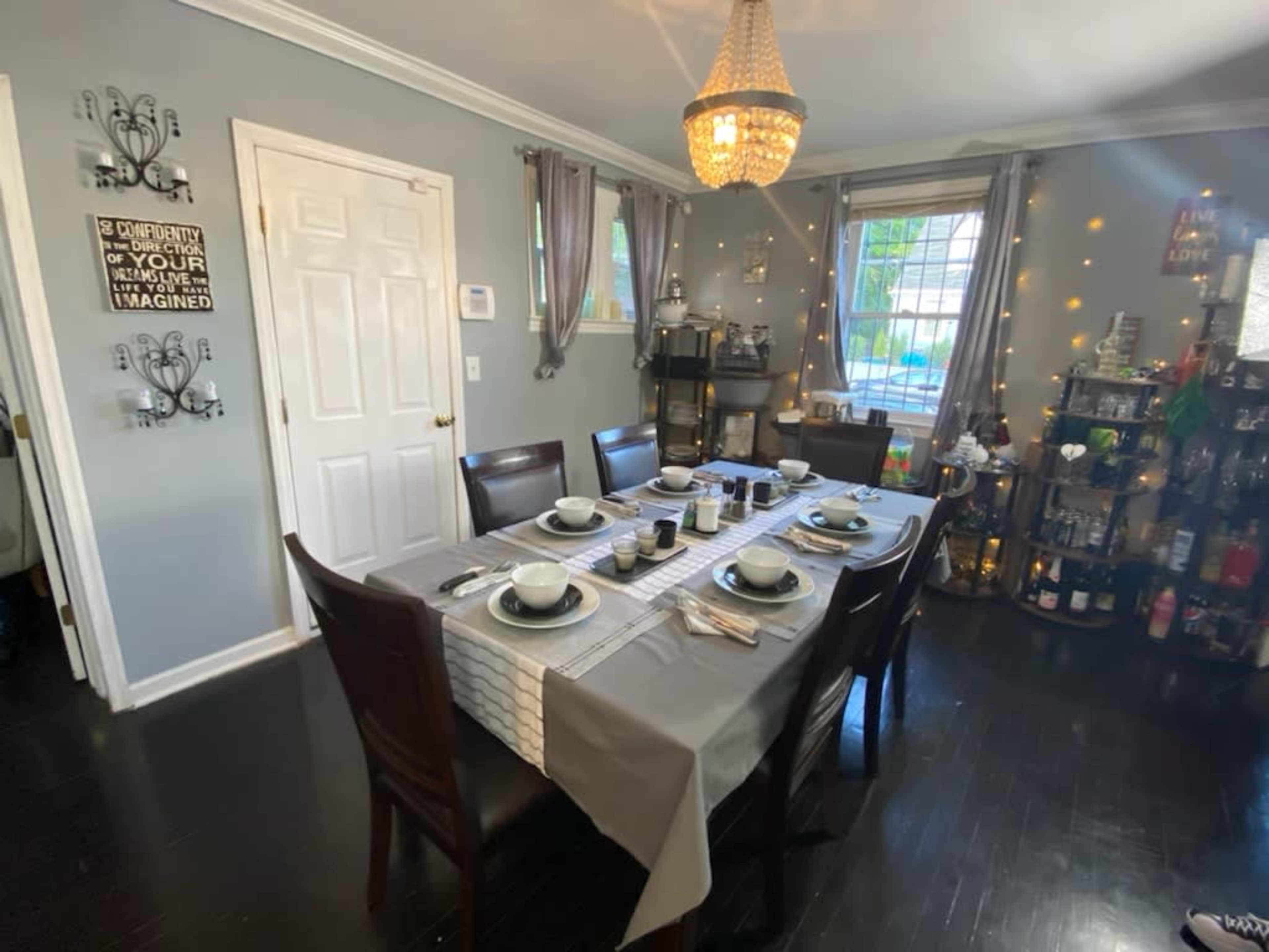 The dining area features a wooden table set for six, adorned with dishes and utensils, and is illuminated by a chandelier and wall-mounted decorations.
