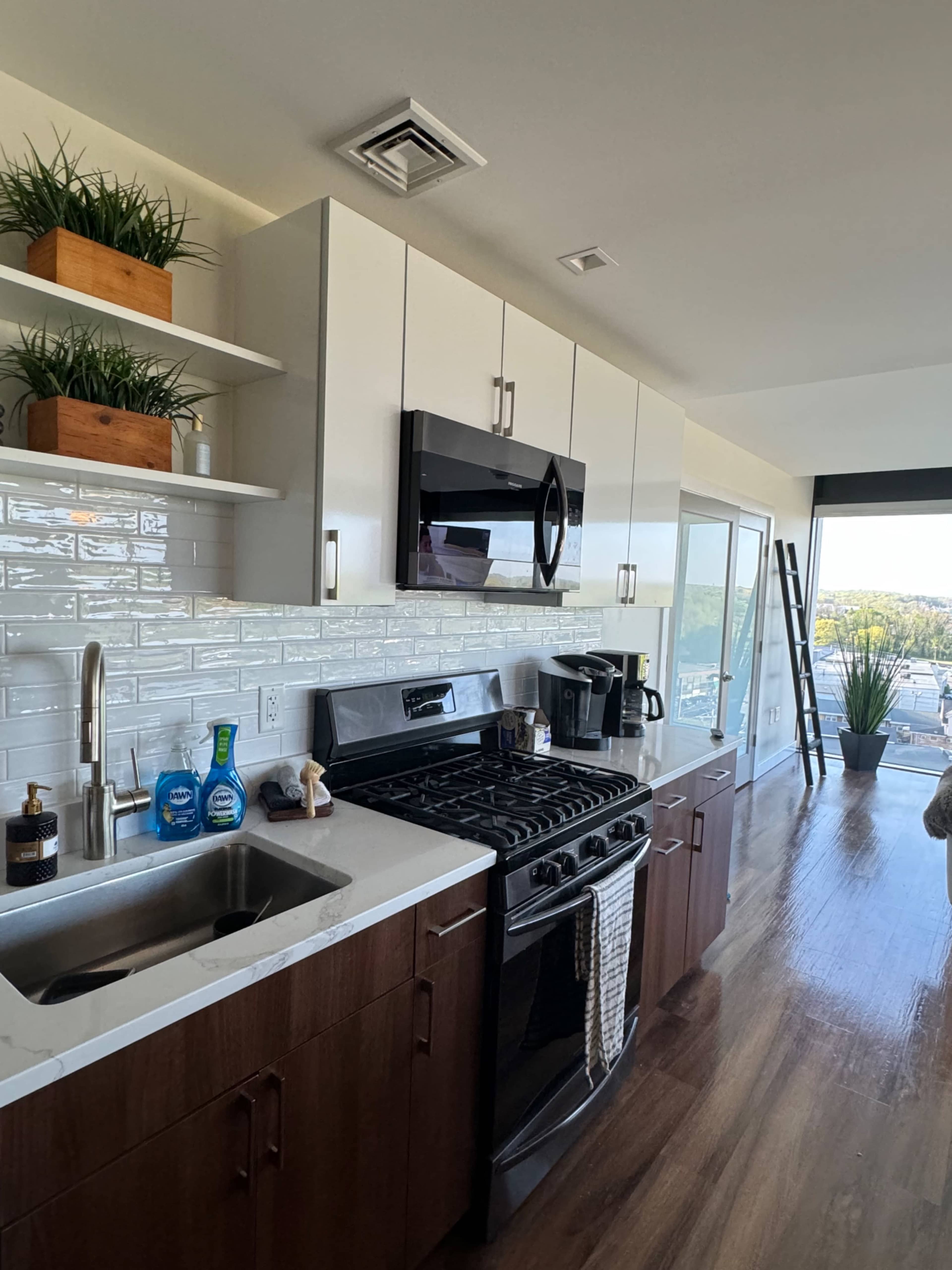 A modern kitchen features white cabinetry, a gas stove, and a stainless-steel sink with a view of the outdoors.