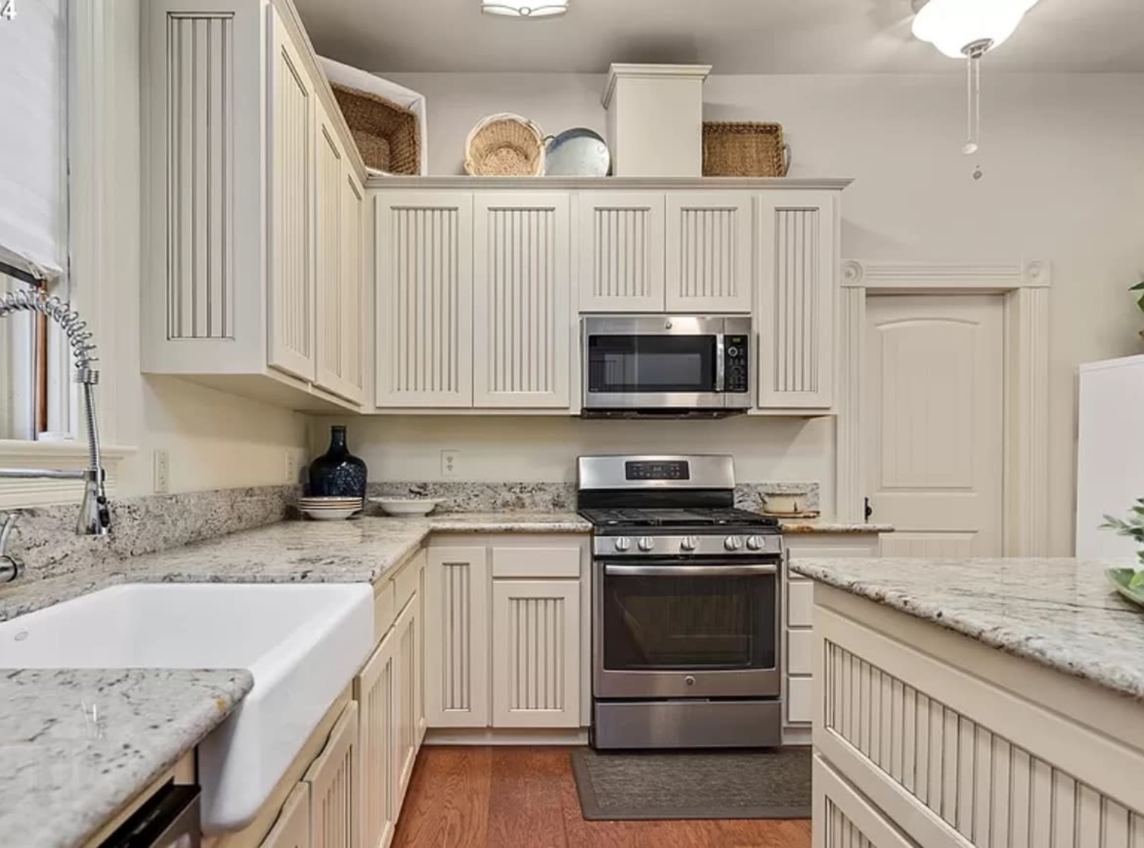 A kitchen with beige cabinetry, granite countertops, a stainless steel oven, and a farmhouse sink.