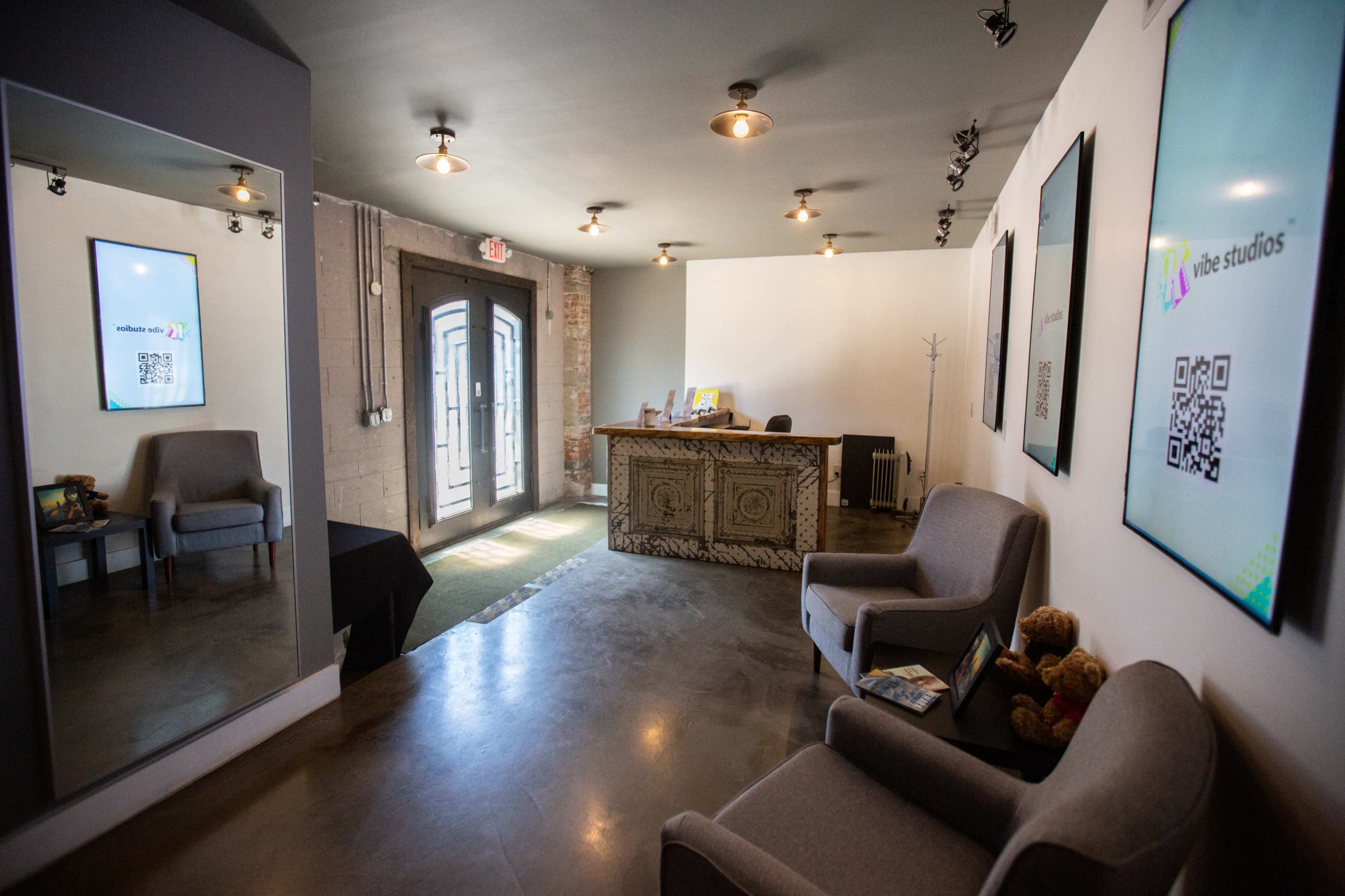 A modern reception area with two gray chairs, a decorative front desk, and digital displays on the walls.