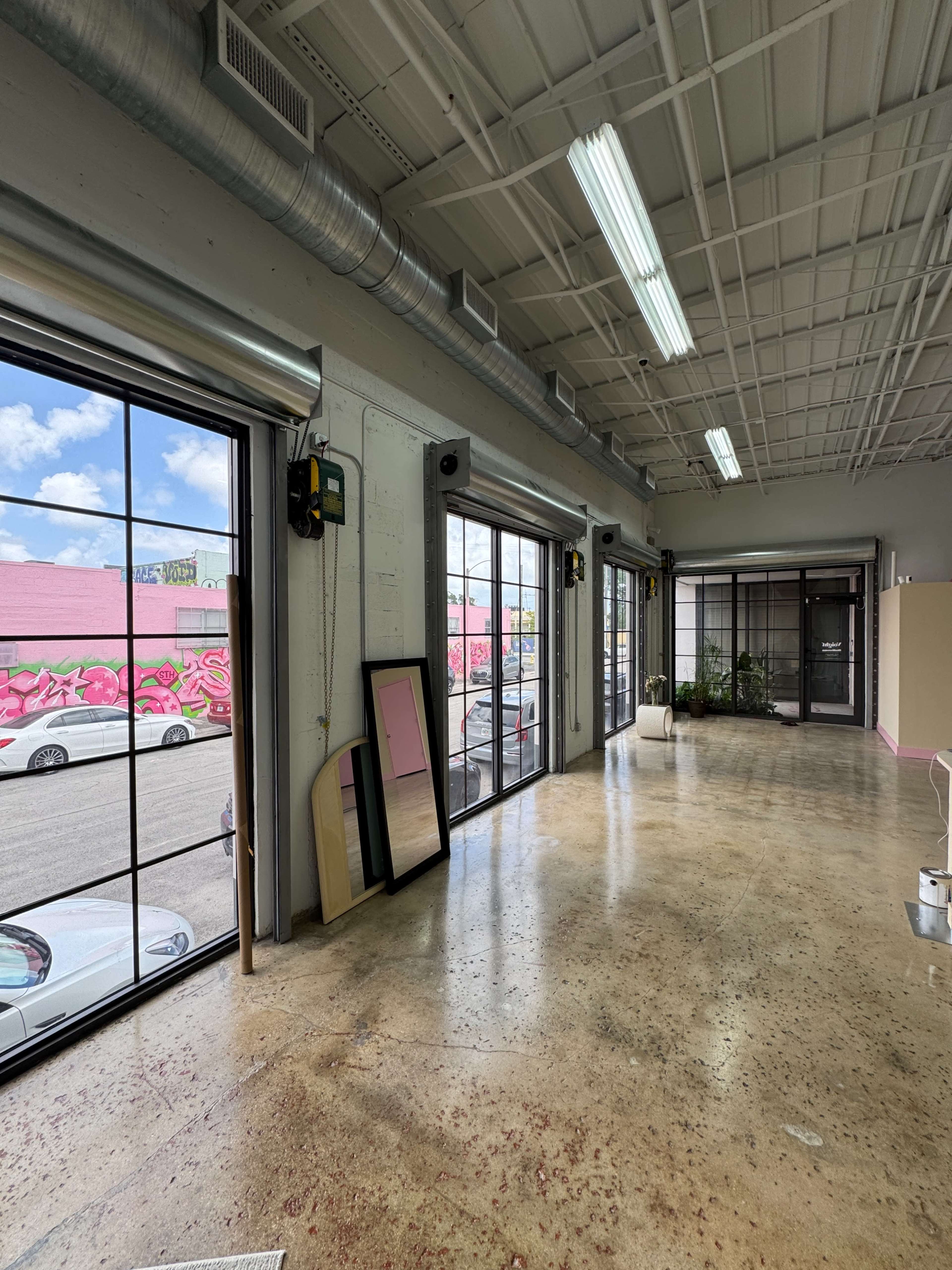 The image shows a spacious interior with large windows, polished concrete floors, and a mural visible through the windows.
