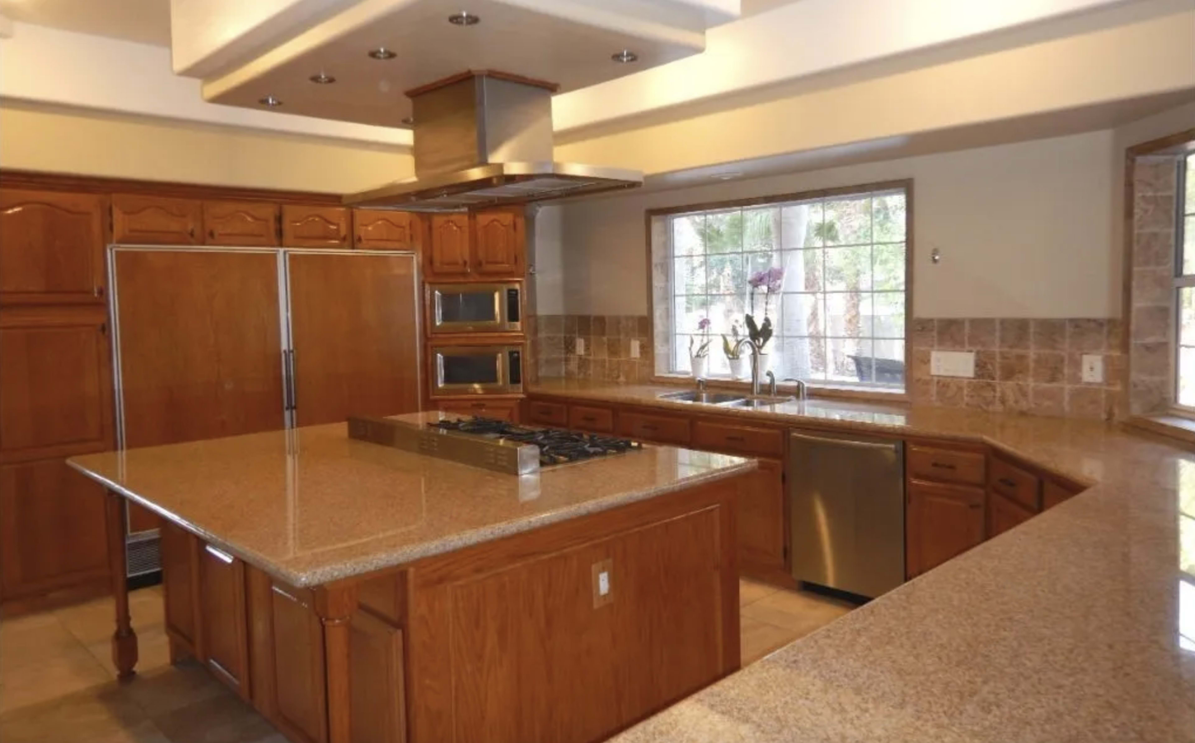 The kitchen features wooden cabinets, a central island with a gas cooktop, and stainless steel appliances under a modern ventilation hood.