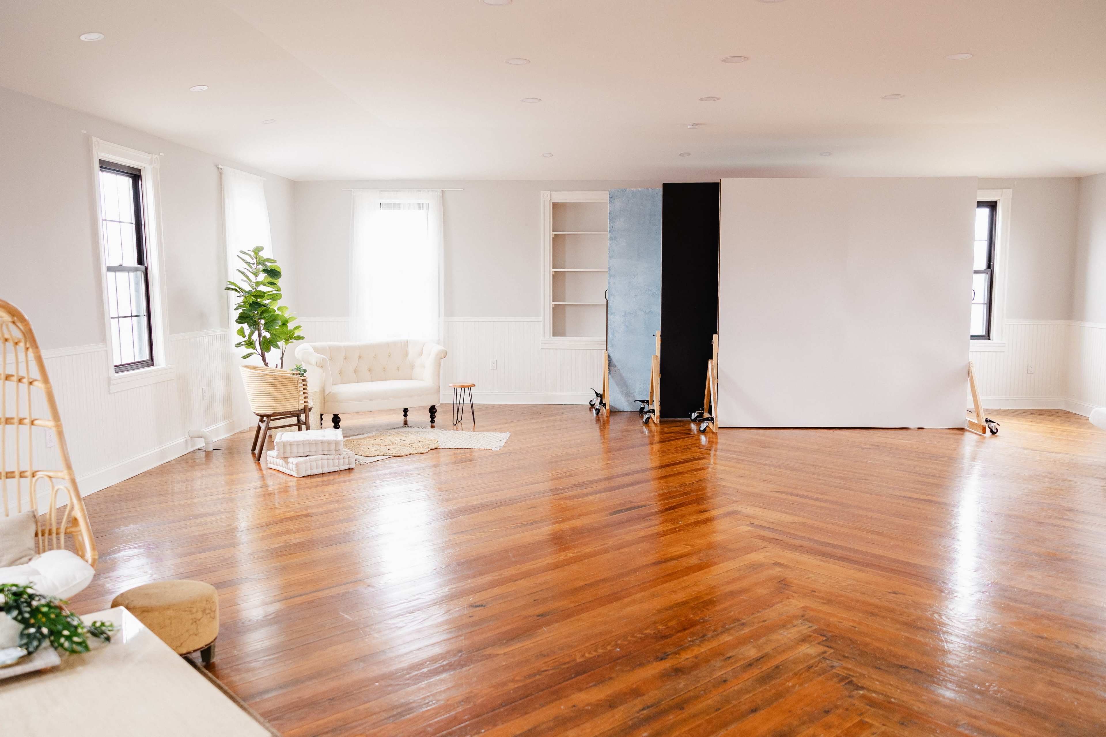 A spacious, well-lit room with wooden flooring and a white couch, featuring a backdrop setup against a wall.