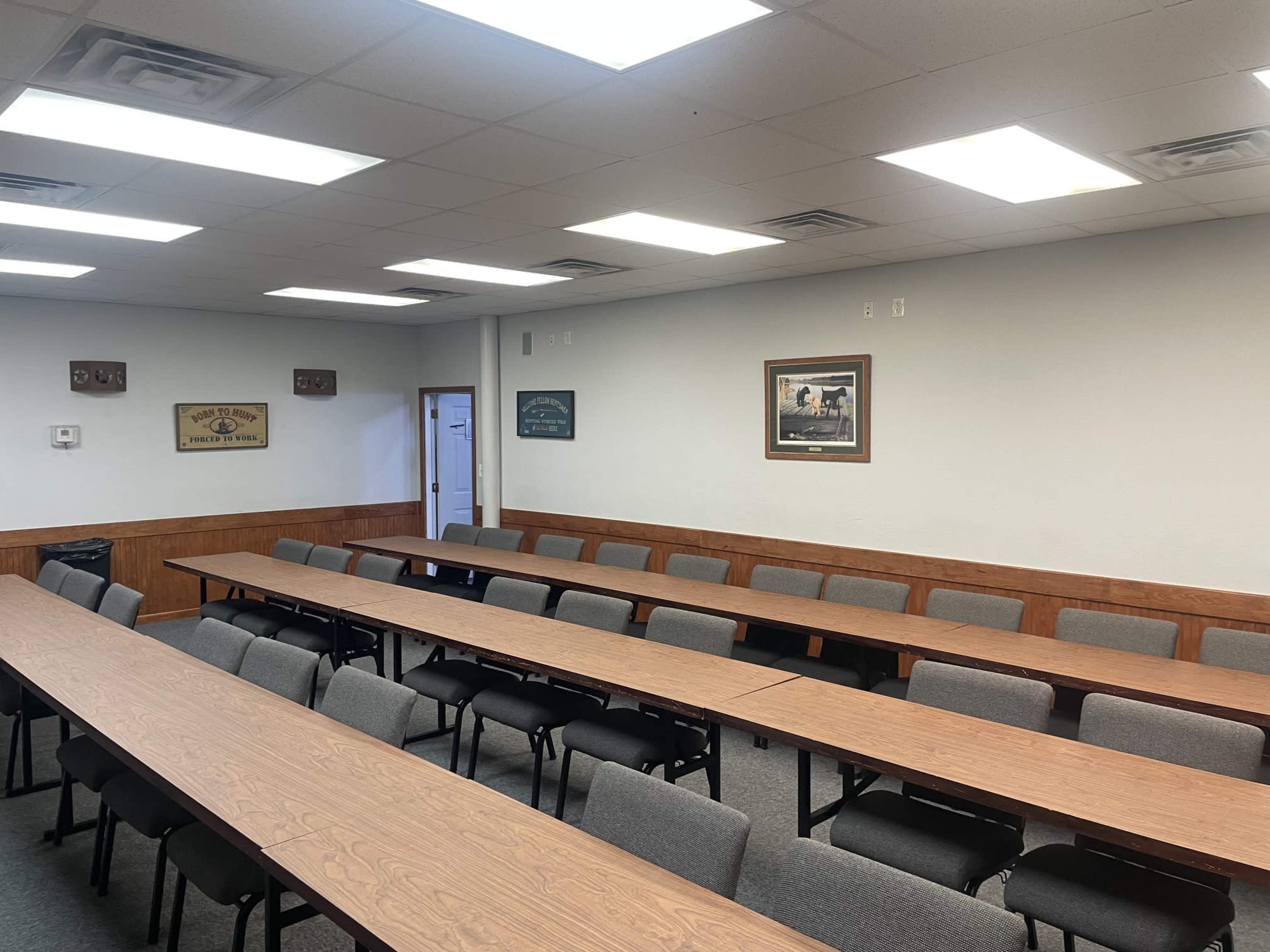 A meeting room features several long tables arranged in rows with chairs, and a few wall decorations.