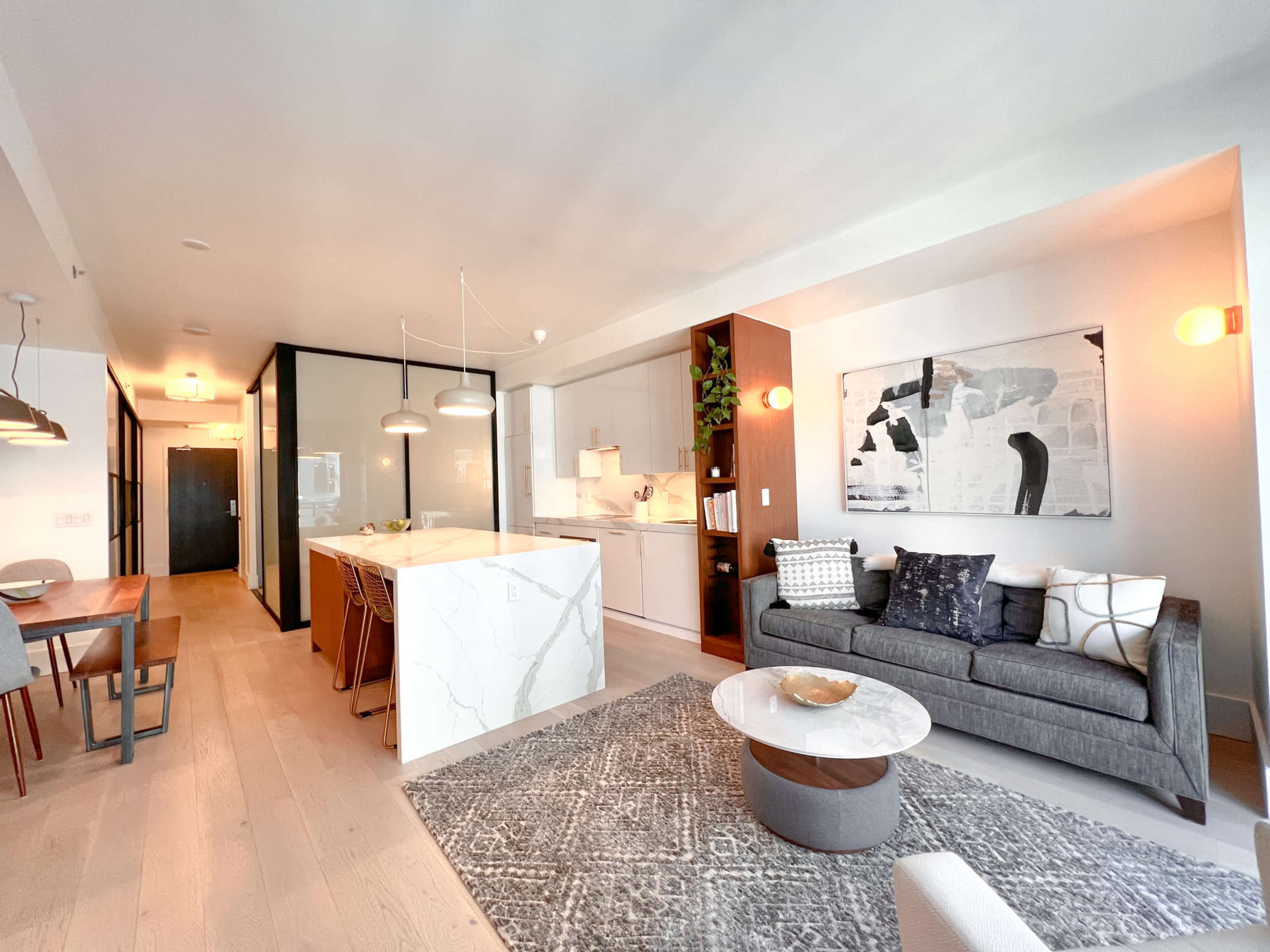 A modern open-concept living space with a kitchen, dining area, and a cozy seating arrangement, highlighted by a marble island and a decorative rug.