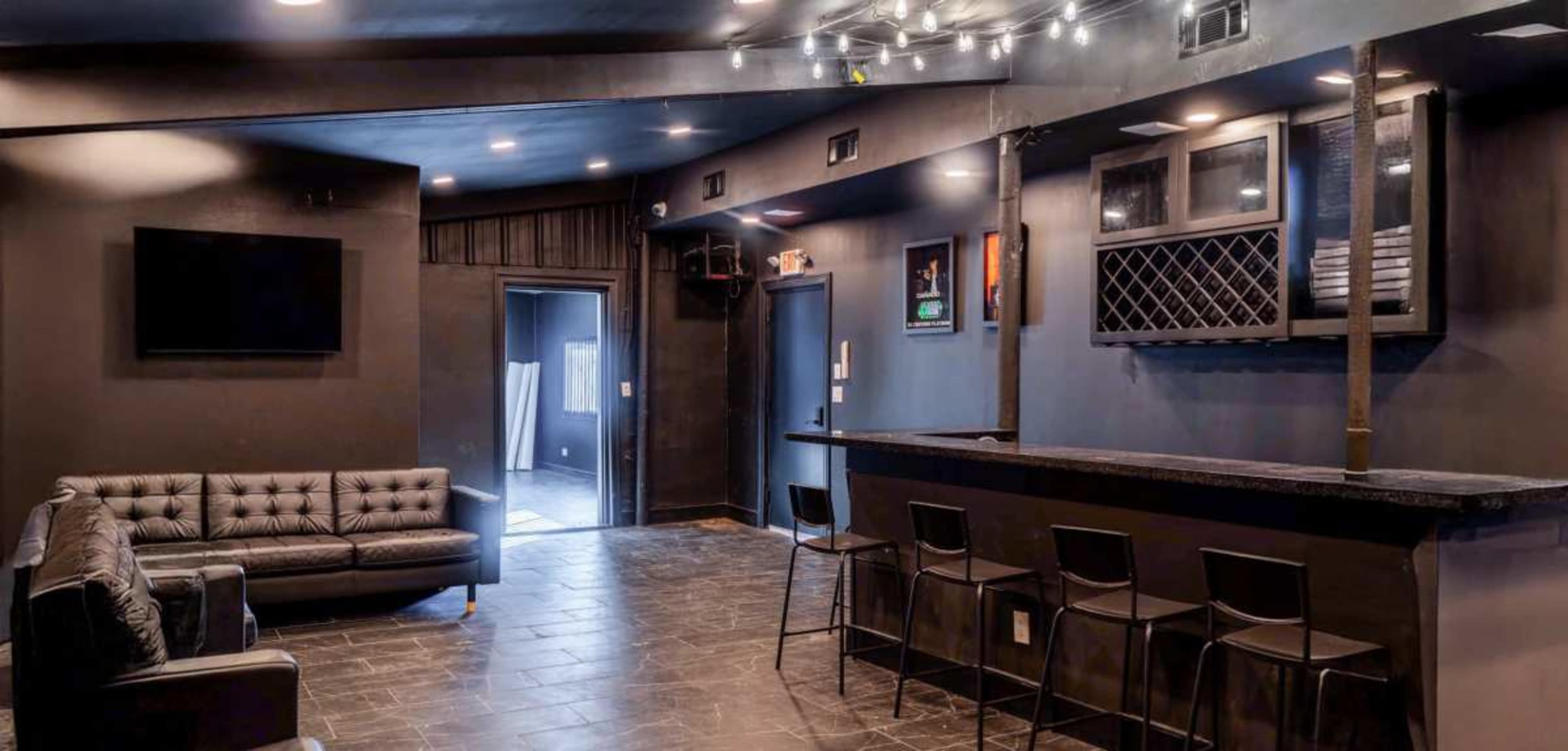 A dark-toned lounge area features a black bar, a couch, and a door leading to another room.