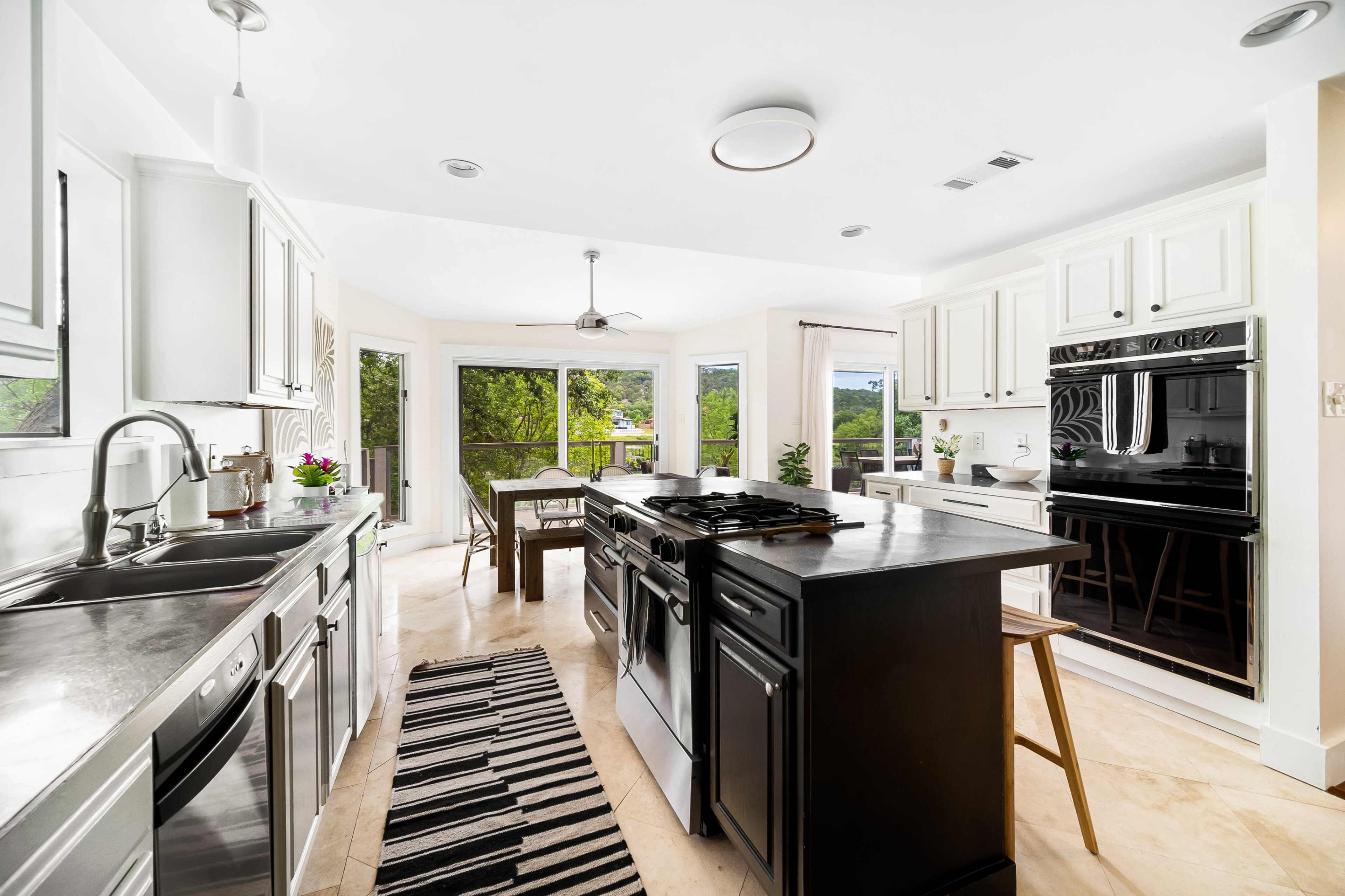 A modern kitchen features stainless steel appliances, white cabinets, and a central island with a black countertop, complemented by large windows offering a view of the outdoors.