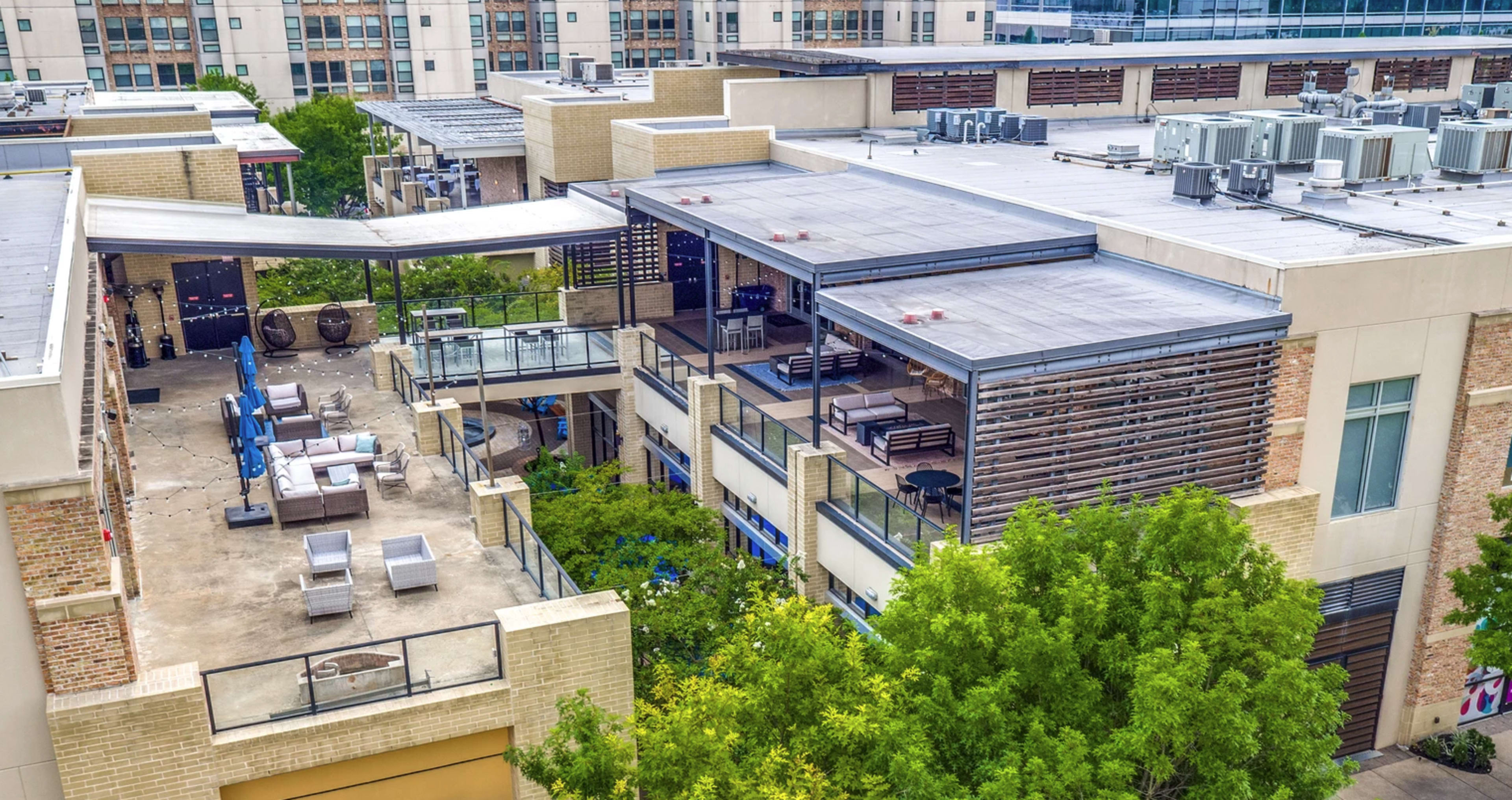 The image shows an urban building complex with multiple levels of outdoor terraces and greenery, featuring modern furniture and air conditioning units on the rooftops.