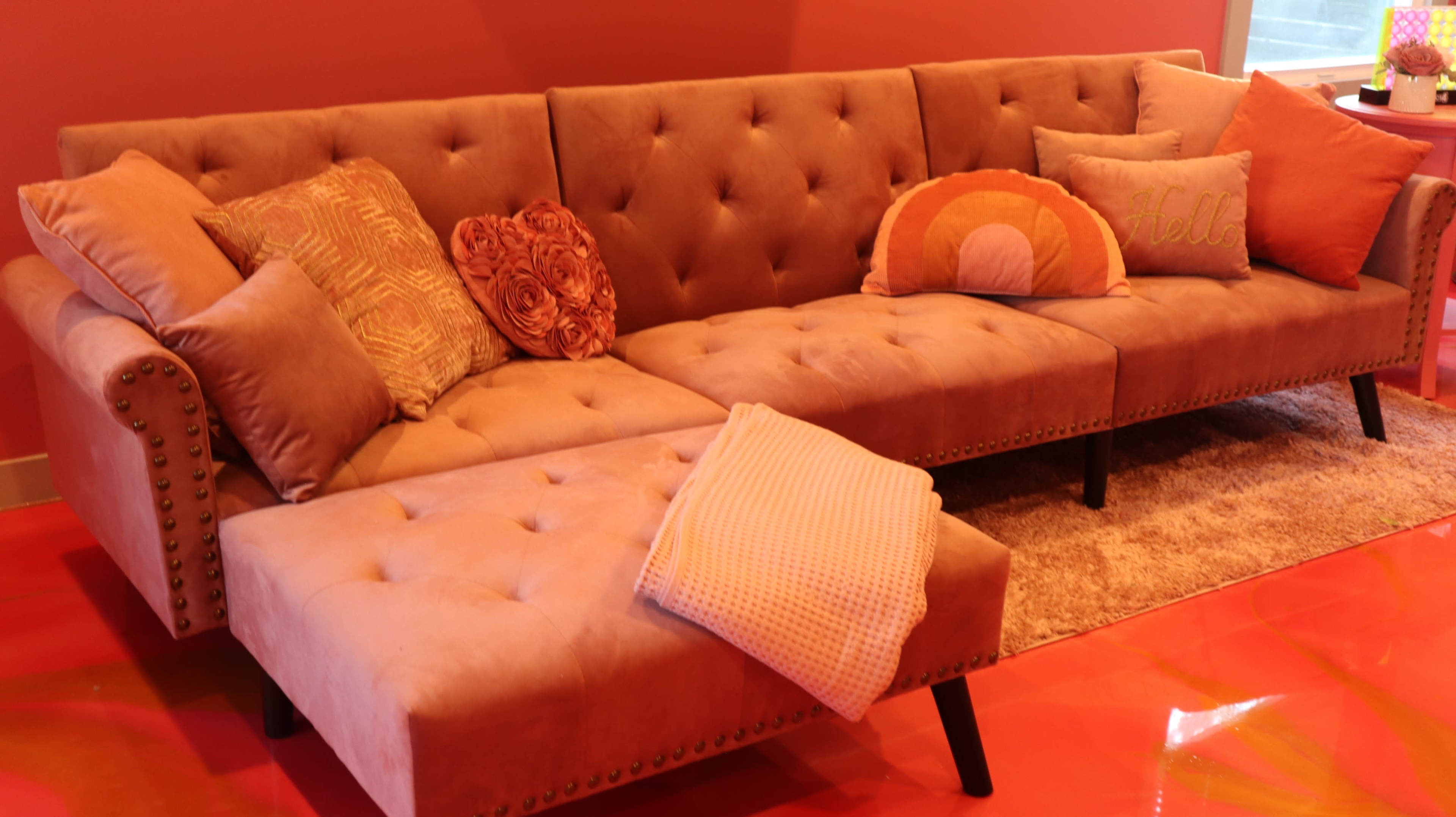 A beige sectional couch with decorative pillows and a thrown blanket is positioned on a glossy red floor.