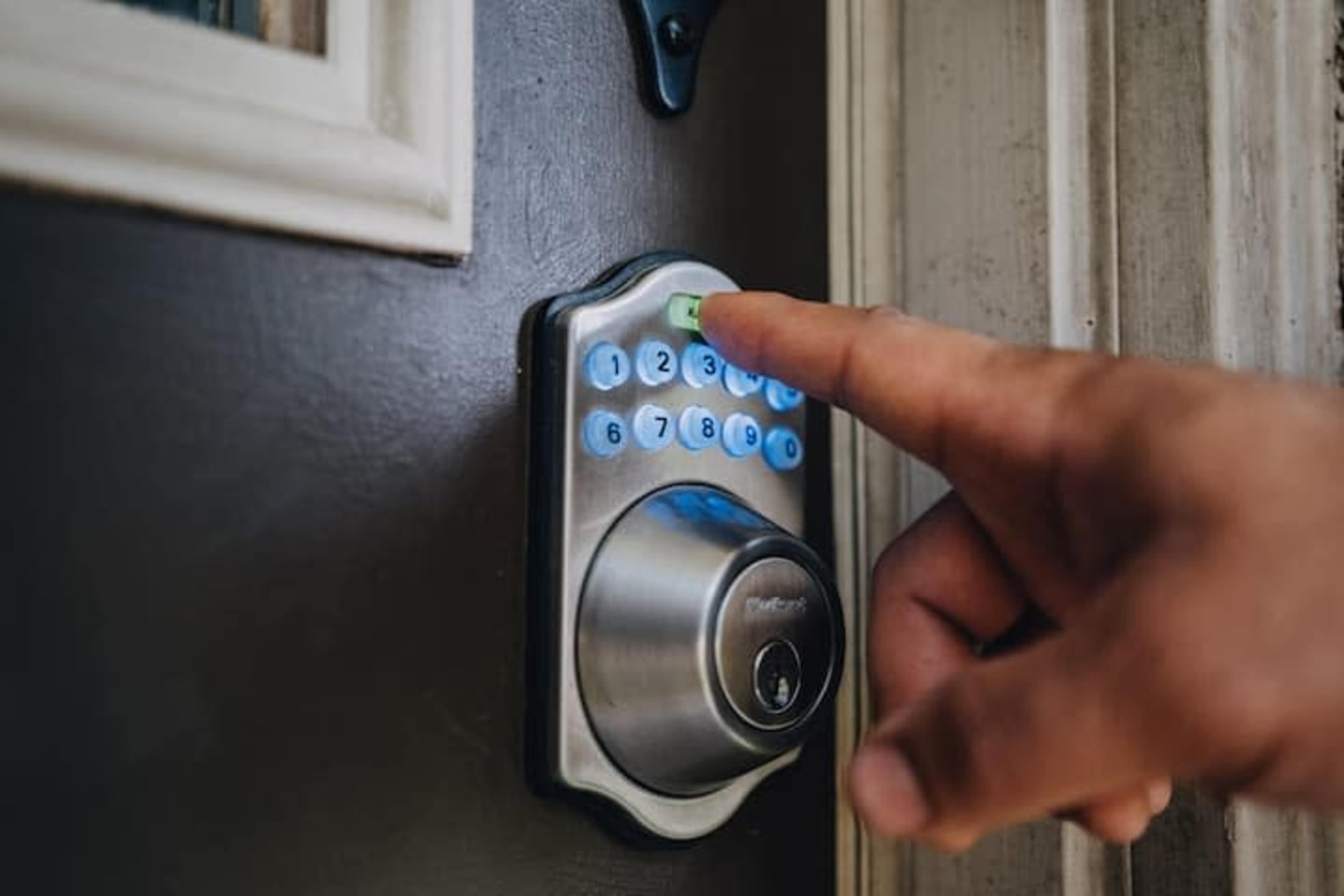 A person is pressing a button on a digital keypad lock installed on a dark wooden door.