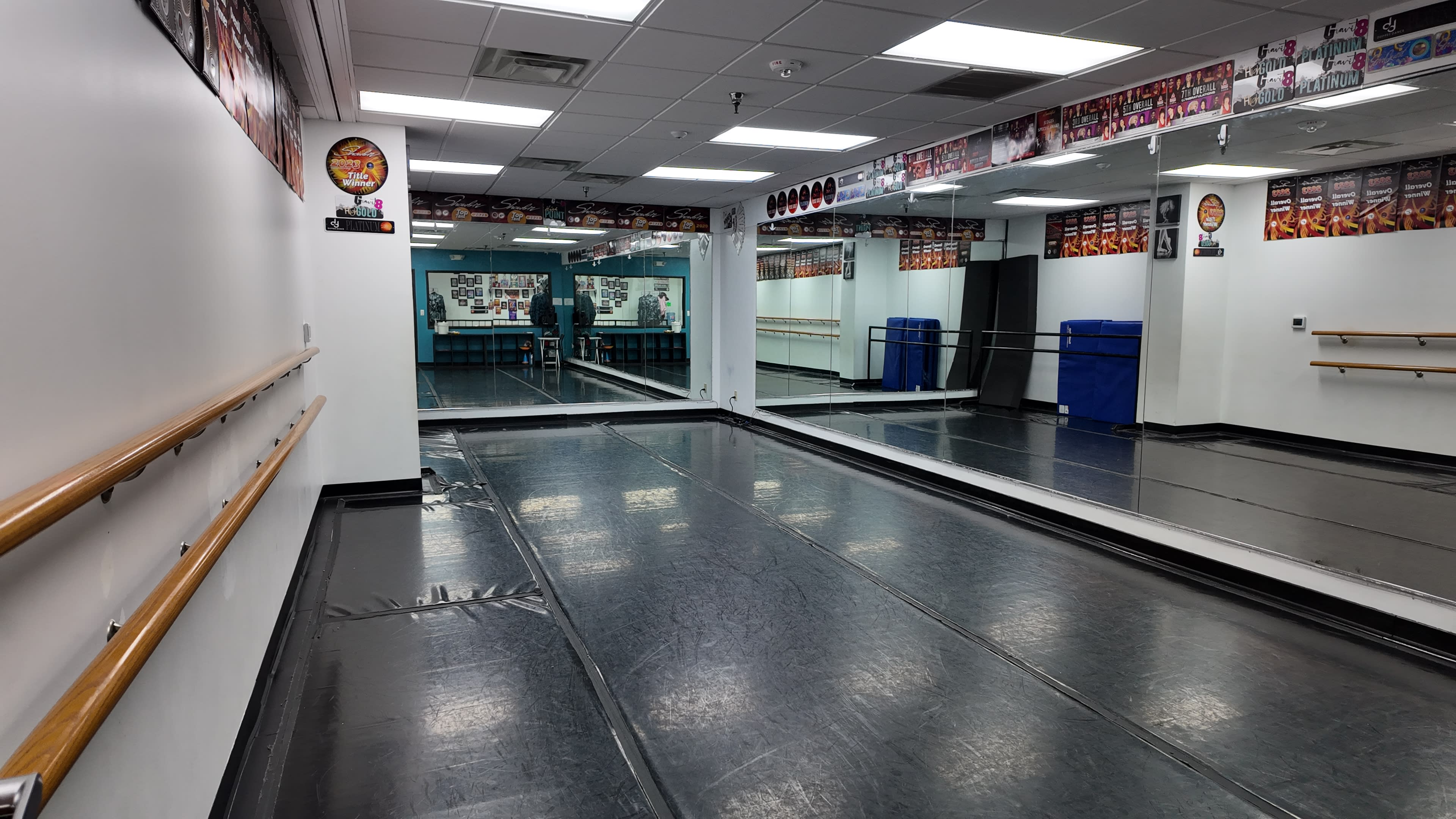 The image shows a dance studio with mirrored walls, a black floor, and a ballet barre along one side.
