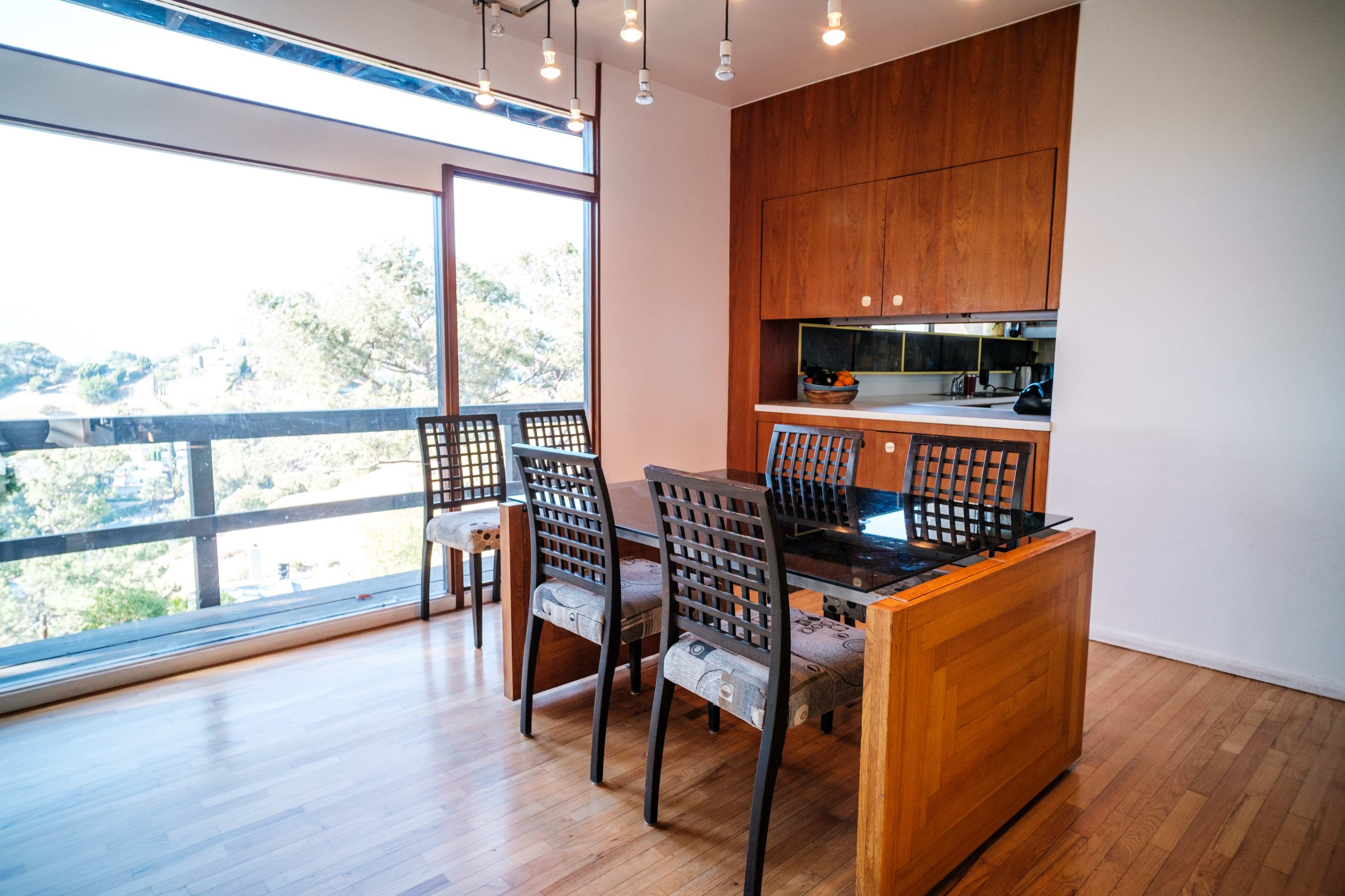 A modern dining area features a wooden table with six black and gray chairs, set against a large window revealing a scenic view.