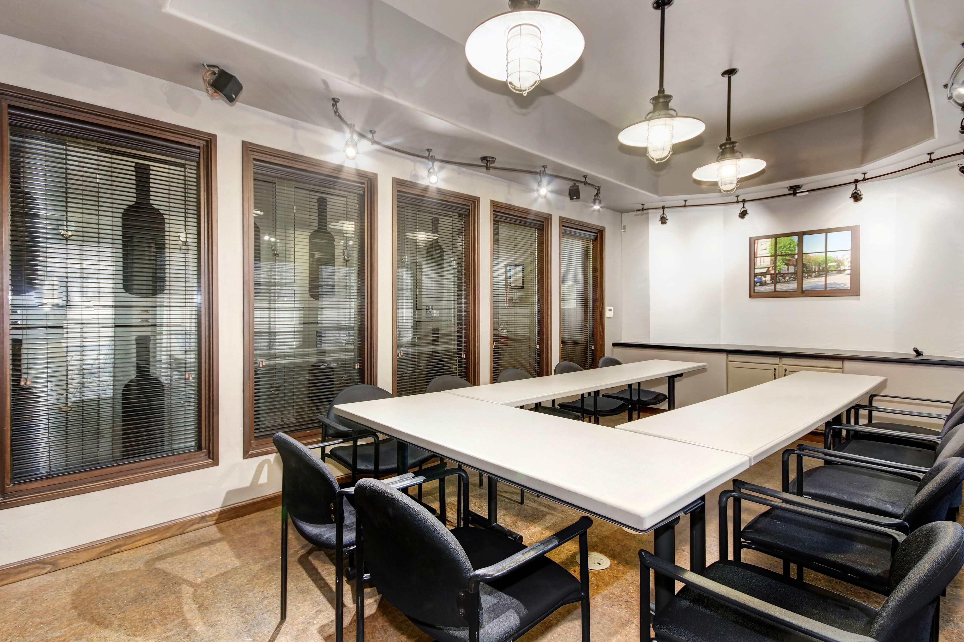 A conference room with a long table surrounded by black chairs, featuring large windows and bottle displays on the walls.