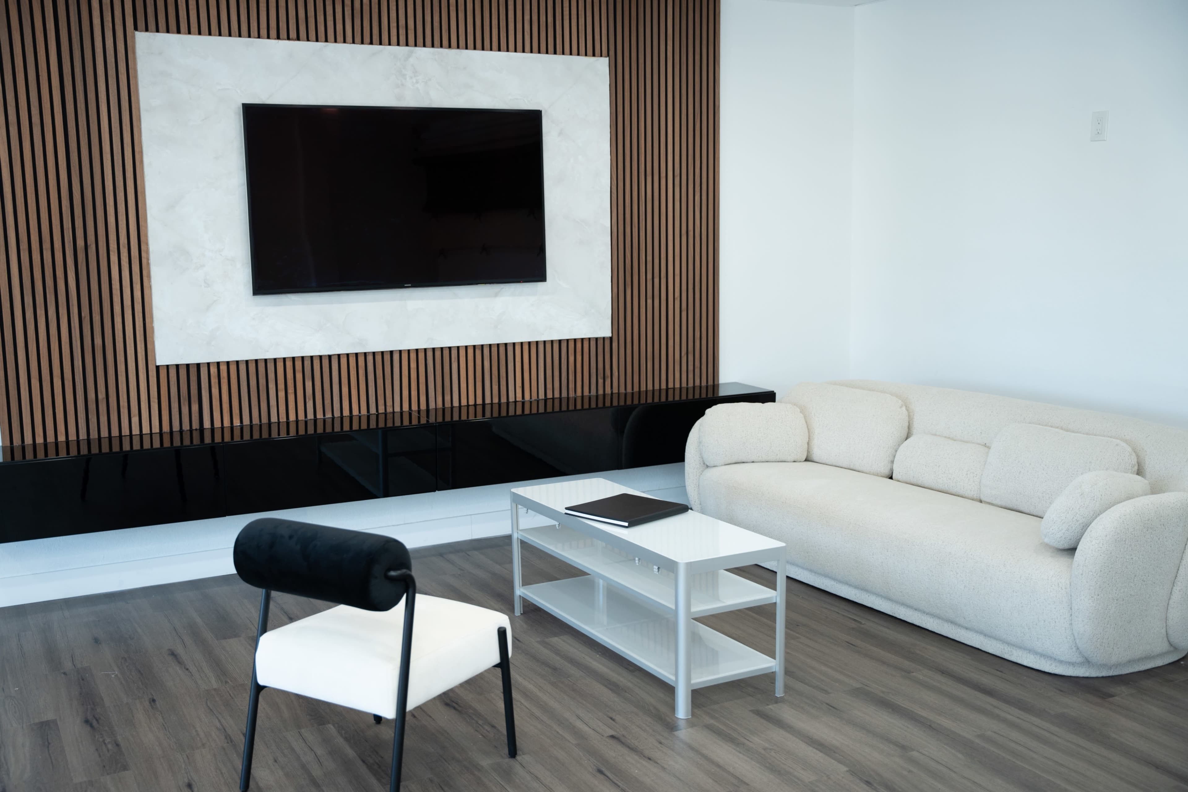 A modern living room with a plush sofa, a small coffee table, and a wall-mounted television framed by a textured panel.