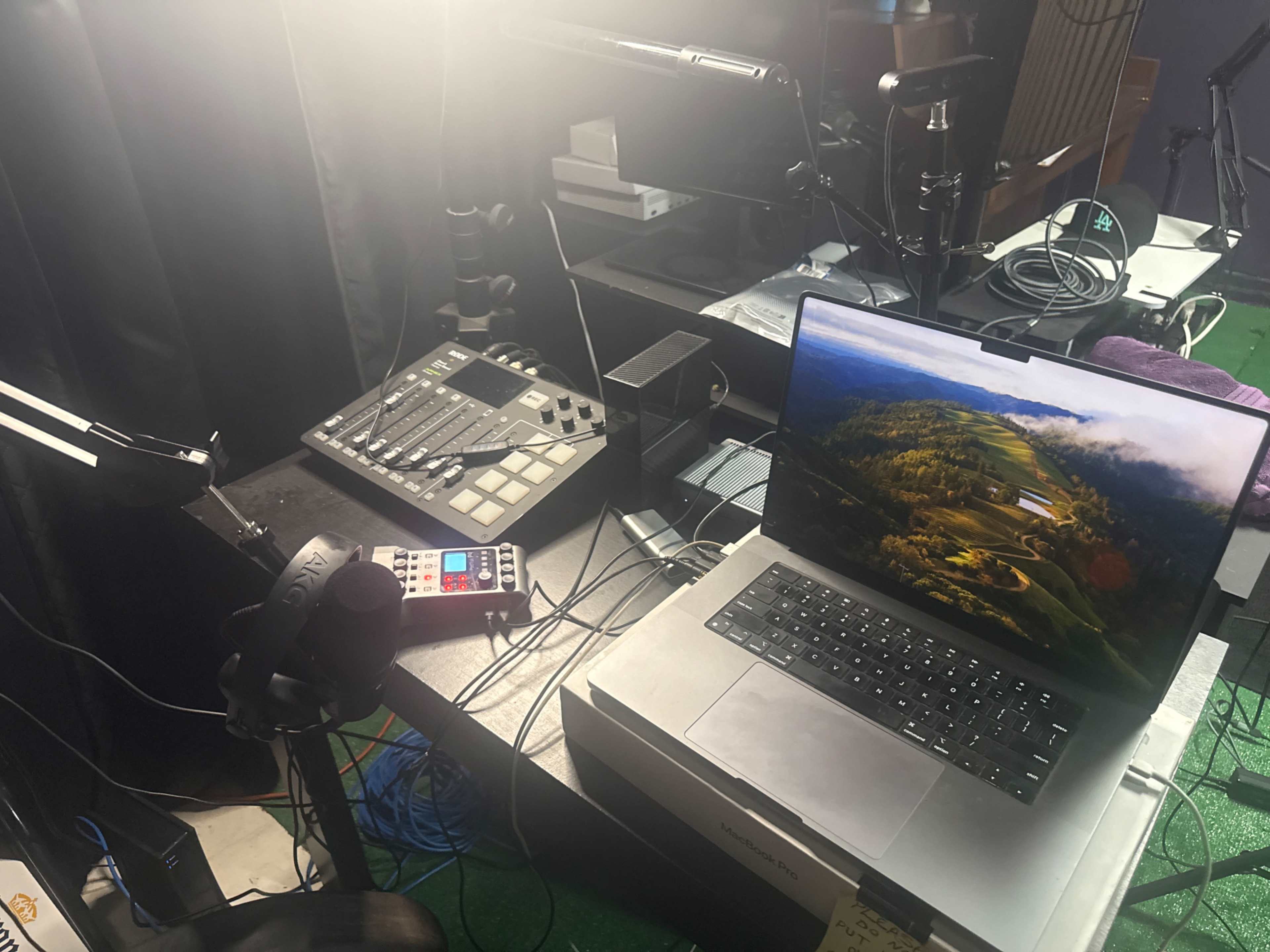 The image shows a workspace with a laptop, a sound mixer, and various cables, all set up in a studio environment.
