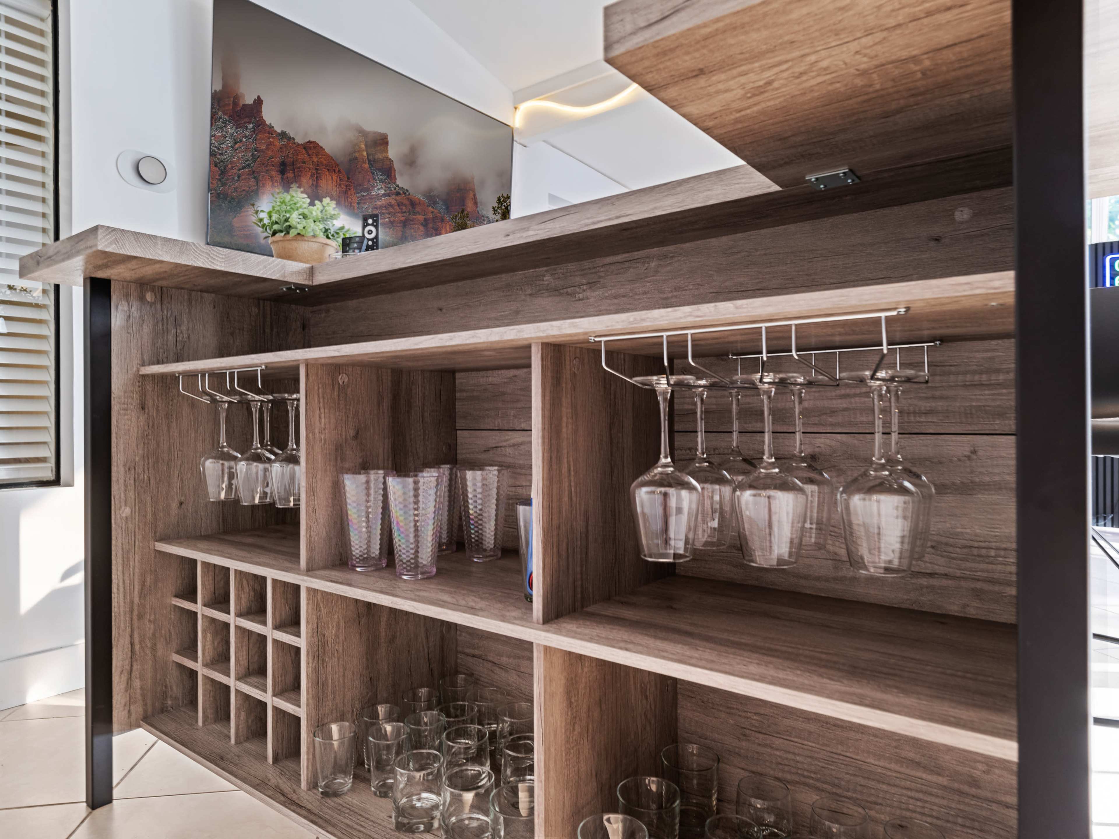 A wooden bar with hanging wine glasses, a storage area for bottles, and a display of clear drinking glasses.