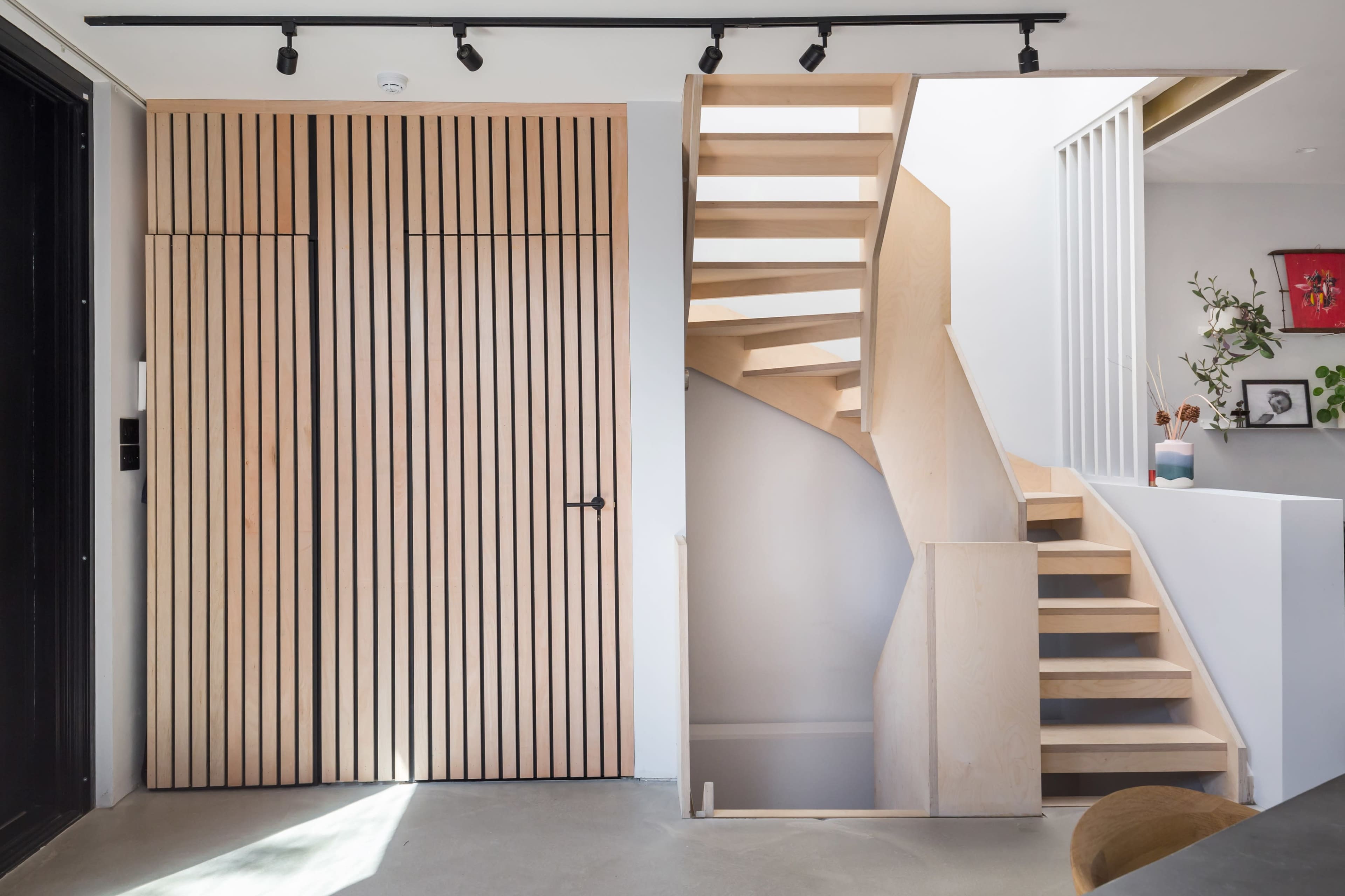 A modern interior space featuring a wooden staircase and a set of vertical slatted wooden doors.