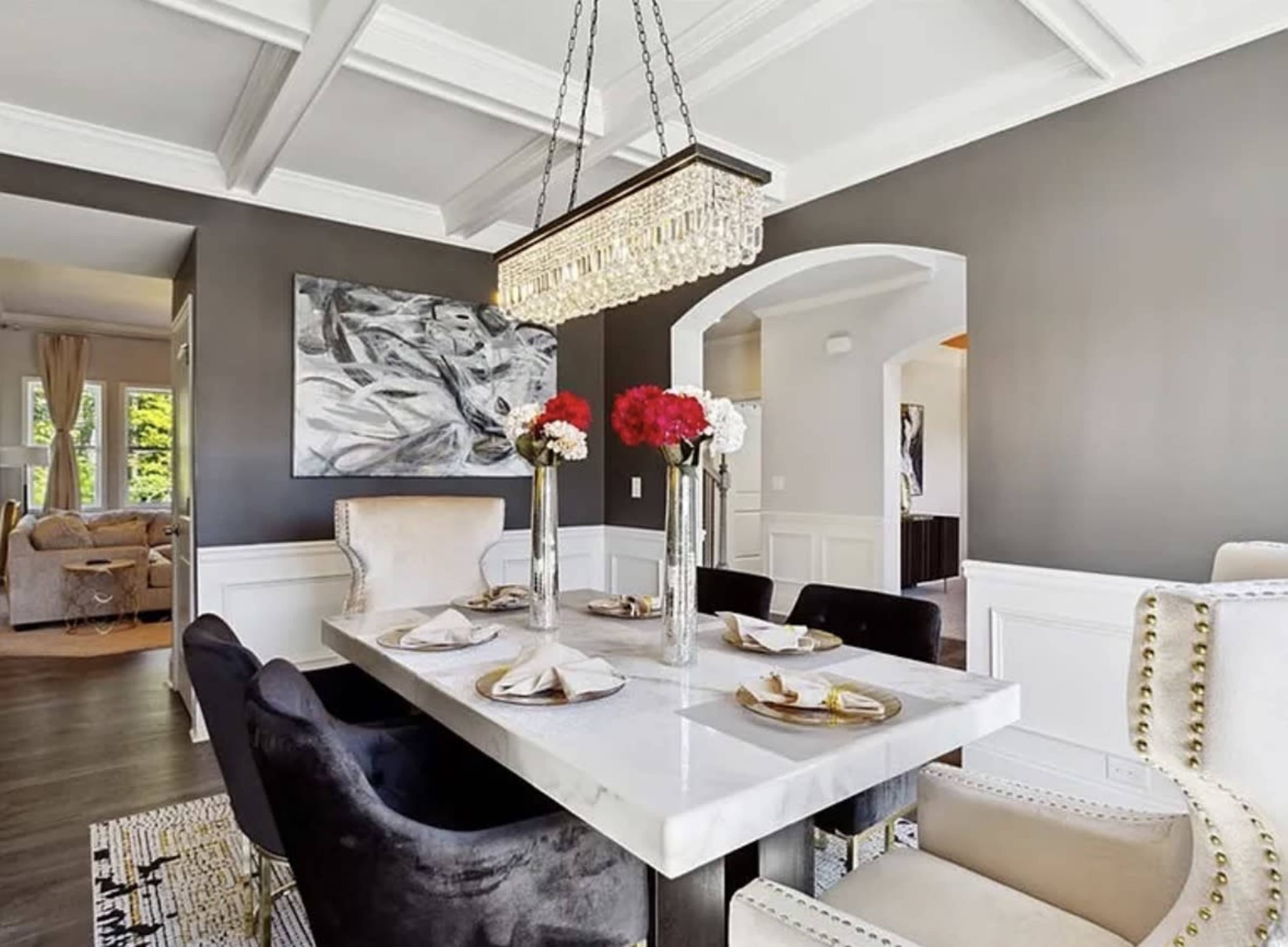The image shows a modern dining room featuring a marble dining table surrounded by black and white chairs, illuminated by a crystal chandelier.