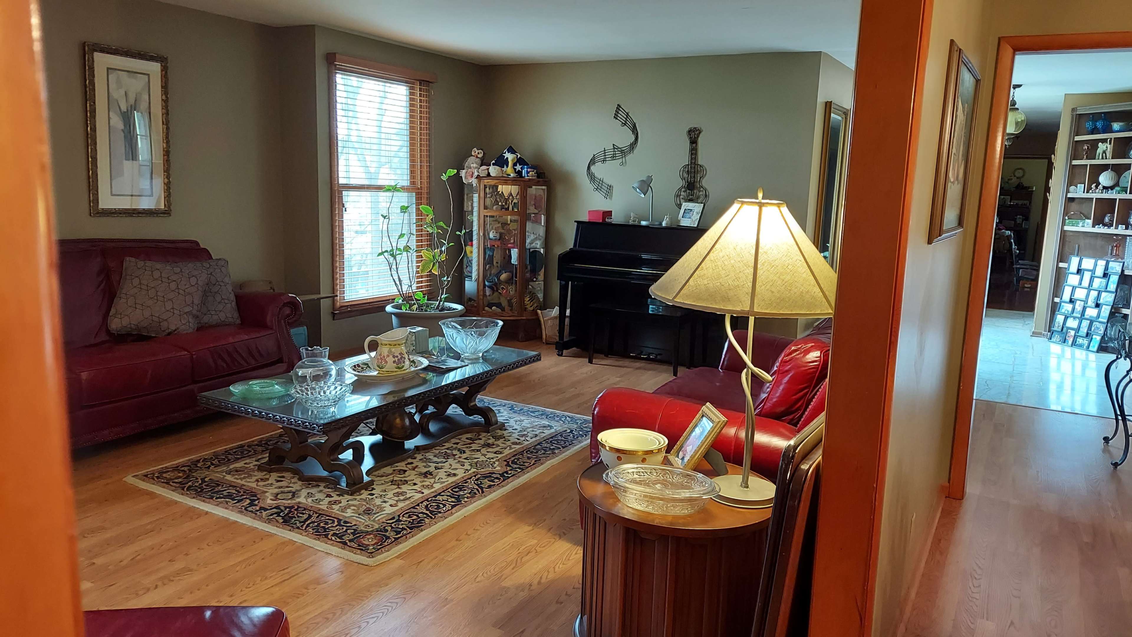A living room with red leather sofas, a wooden coffee table, a piano, and a decorative rug.