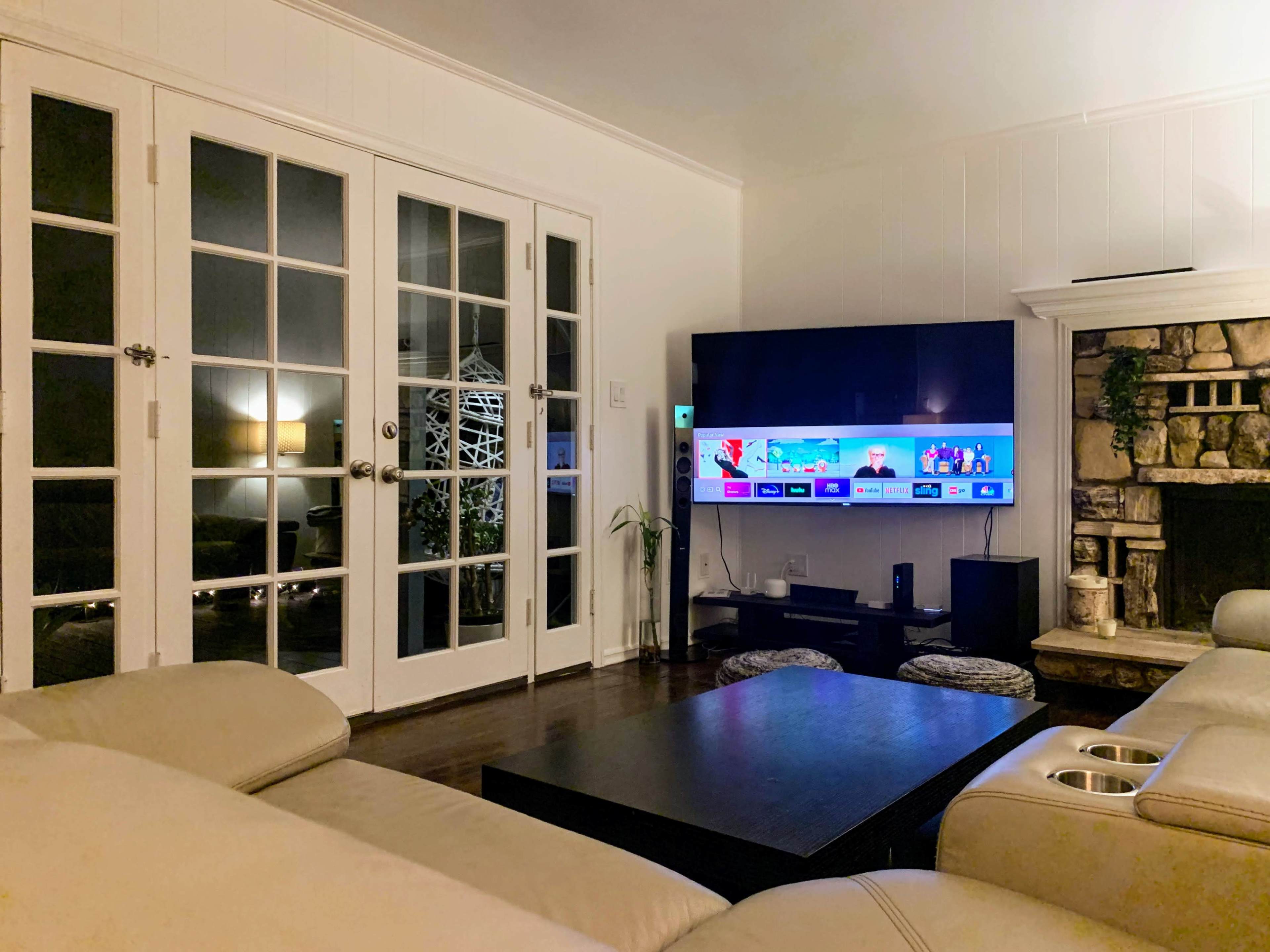 A living room with a flat-screen TV mounted on the wall, a coffee table in front, and French doors leading to another space.