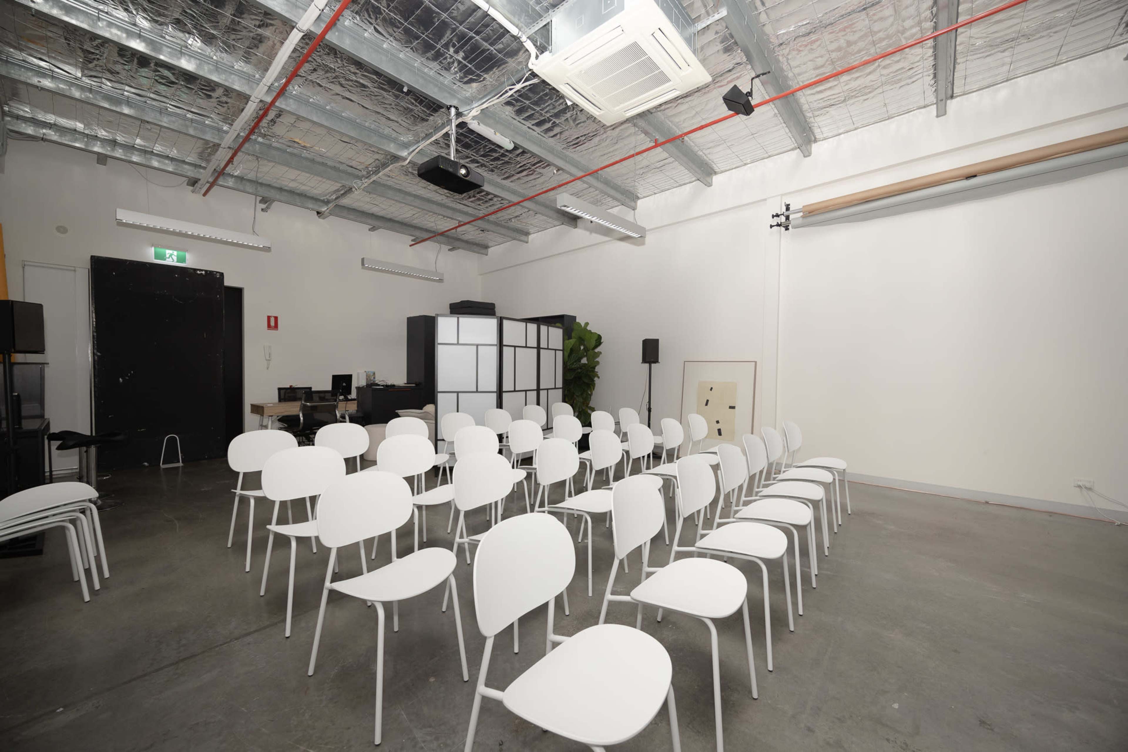 A row of white chairs is arranged in a spacious, well-lit room with a high ceiling and minimal decor.