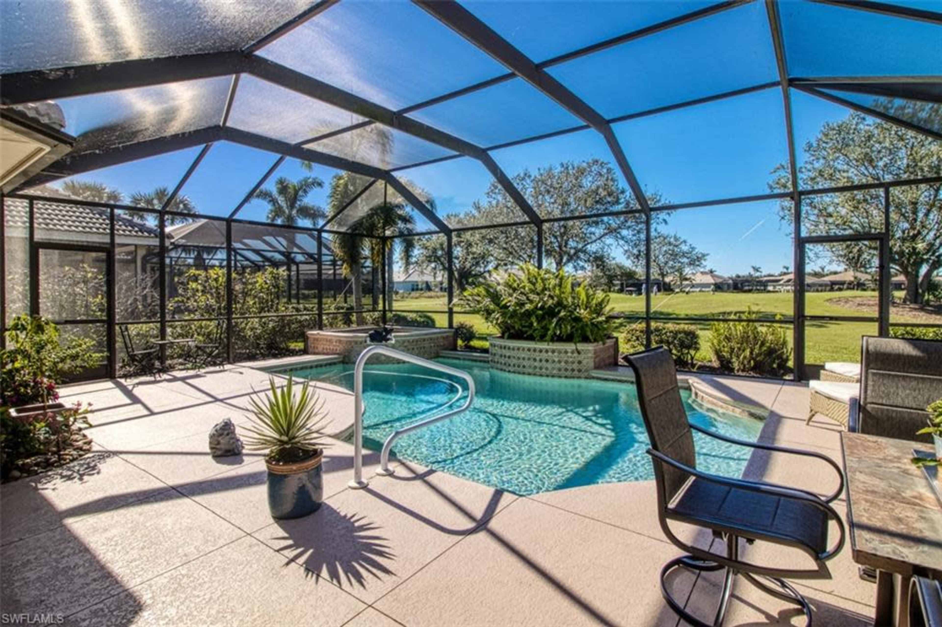A screened-in patio area with a swimming pool, lounge chairs, and a landscaped view of a golf course in the background.