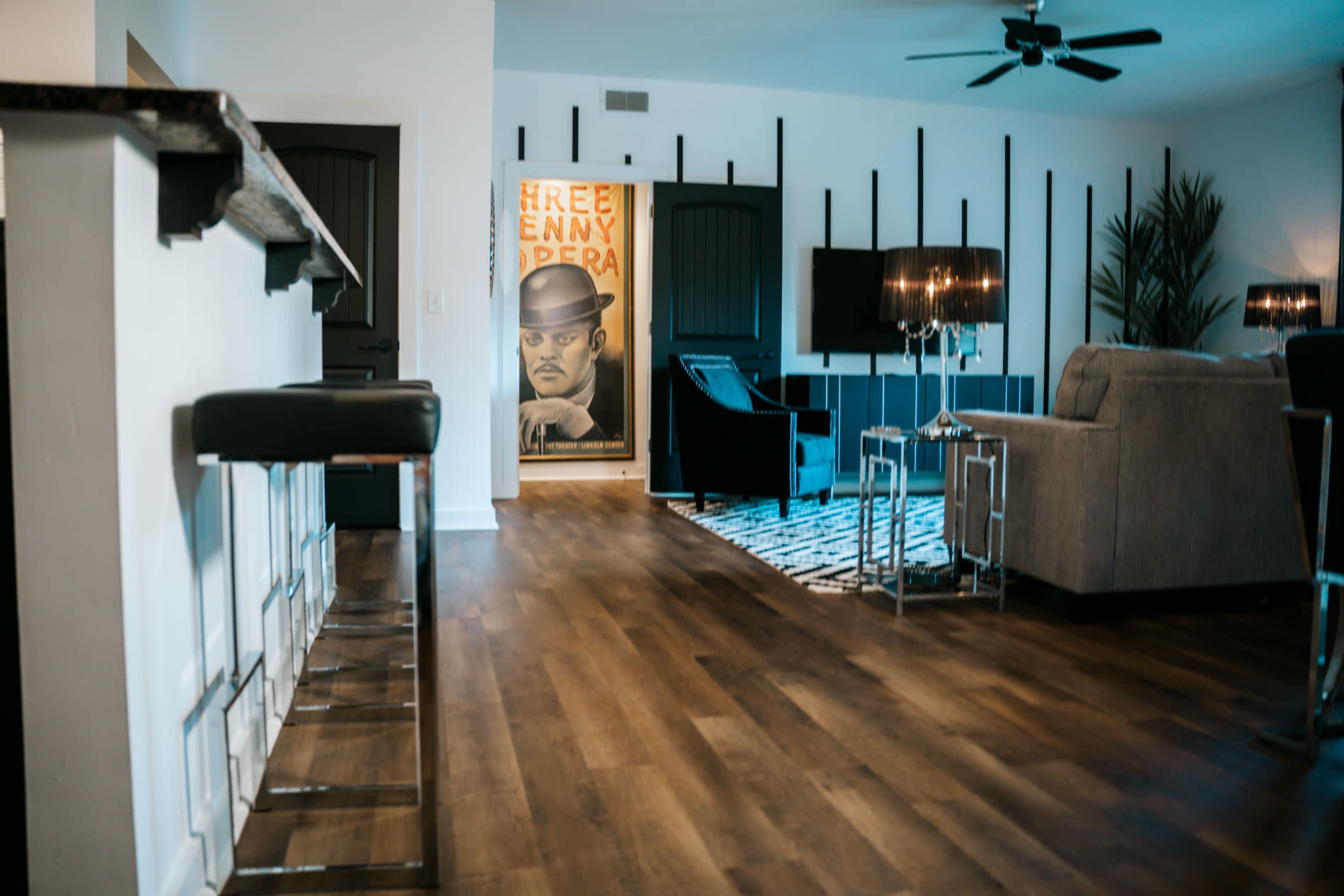 A modern living room with a bar area, a couch, and a large wall mural featuring a man in a hat.
