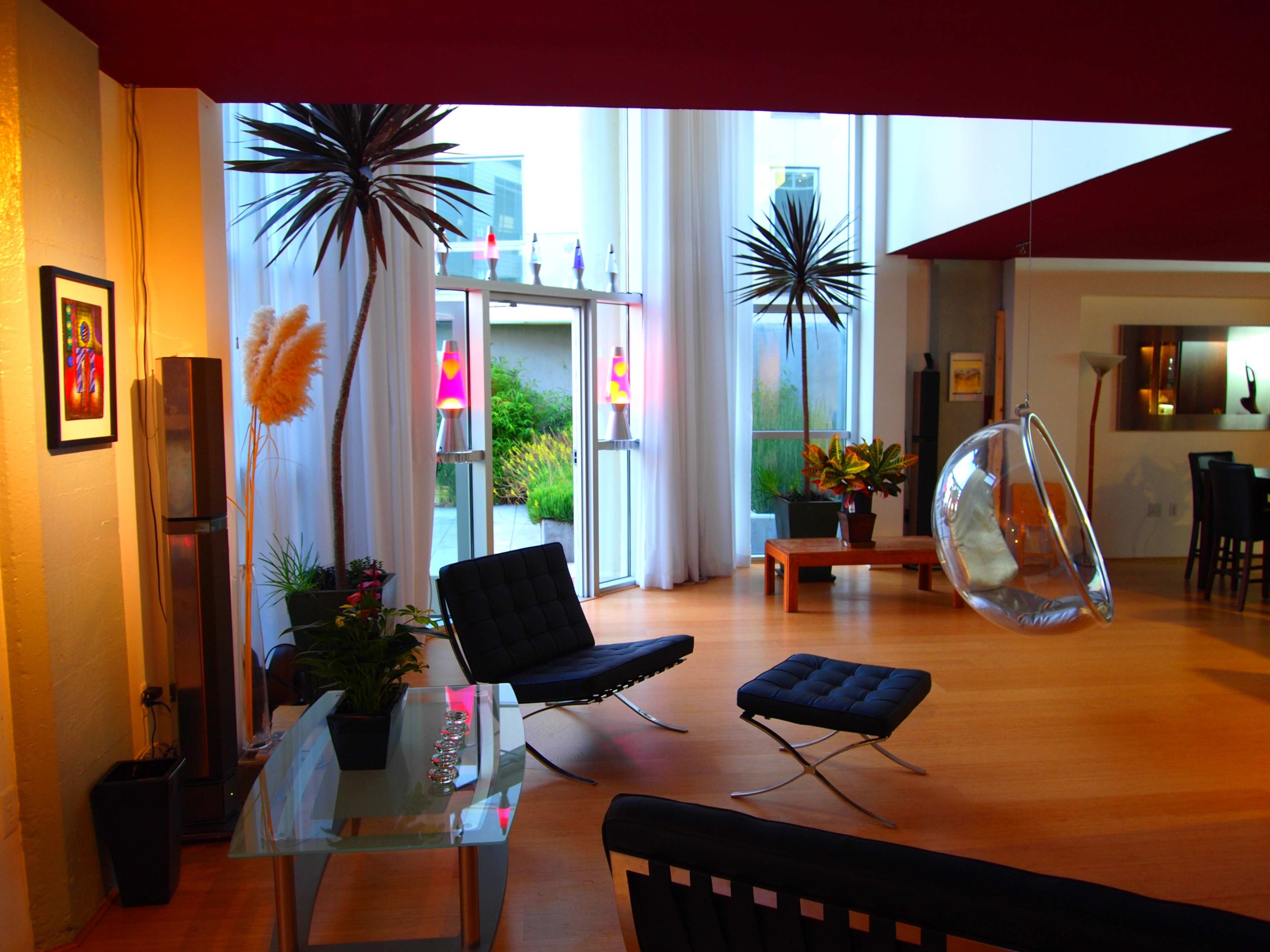A modern living room with a glass table, black chairs, and a hanging chair, featuring large windows that allow natural light to enter the space.