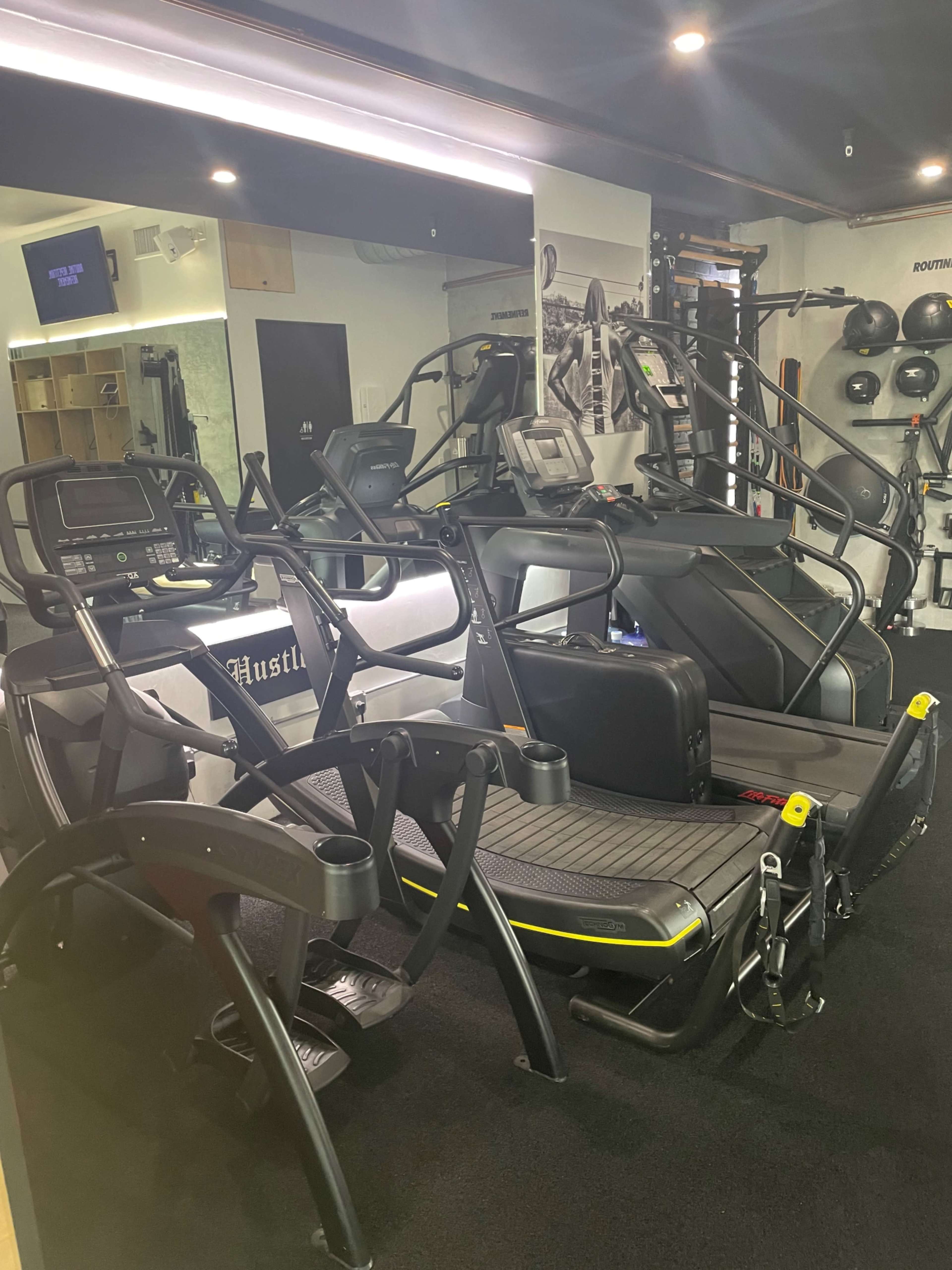 A modern gym interior featuring various exercise machines, including treadmills and an elliptical, against a mirror backdrop.