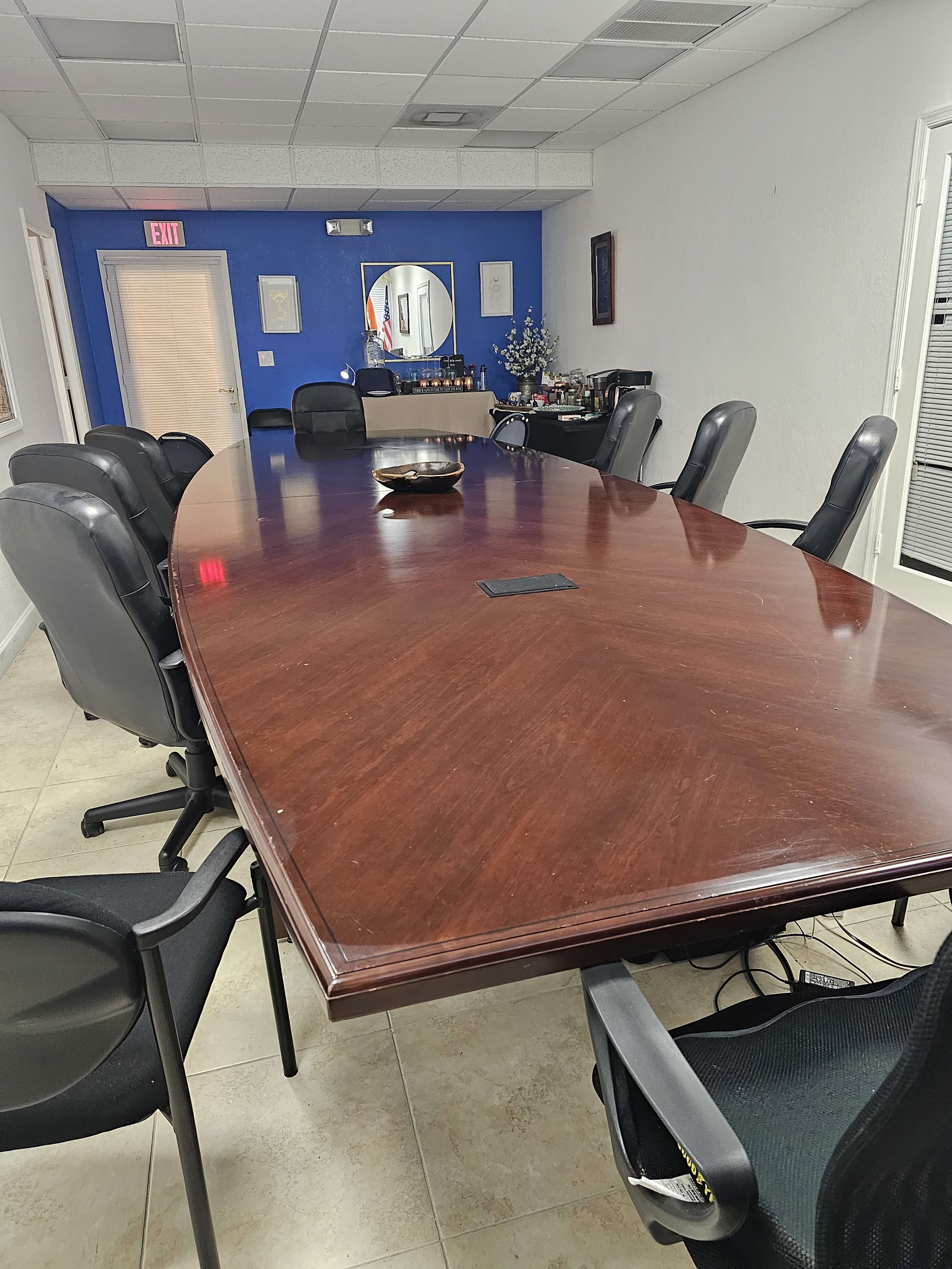 A long, oval wooden conference table is surrounded by black office chairs in a room with blue and white walls.