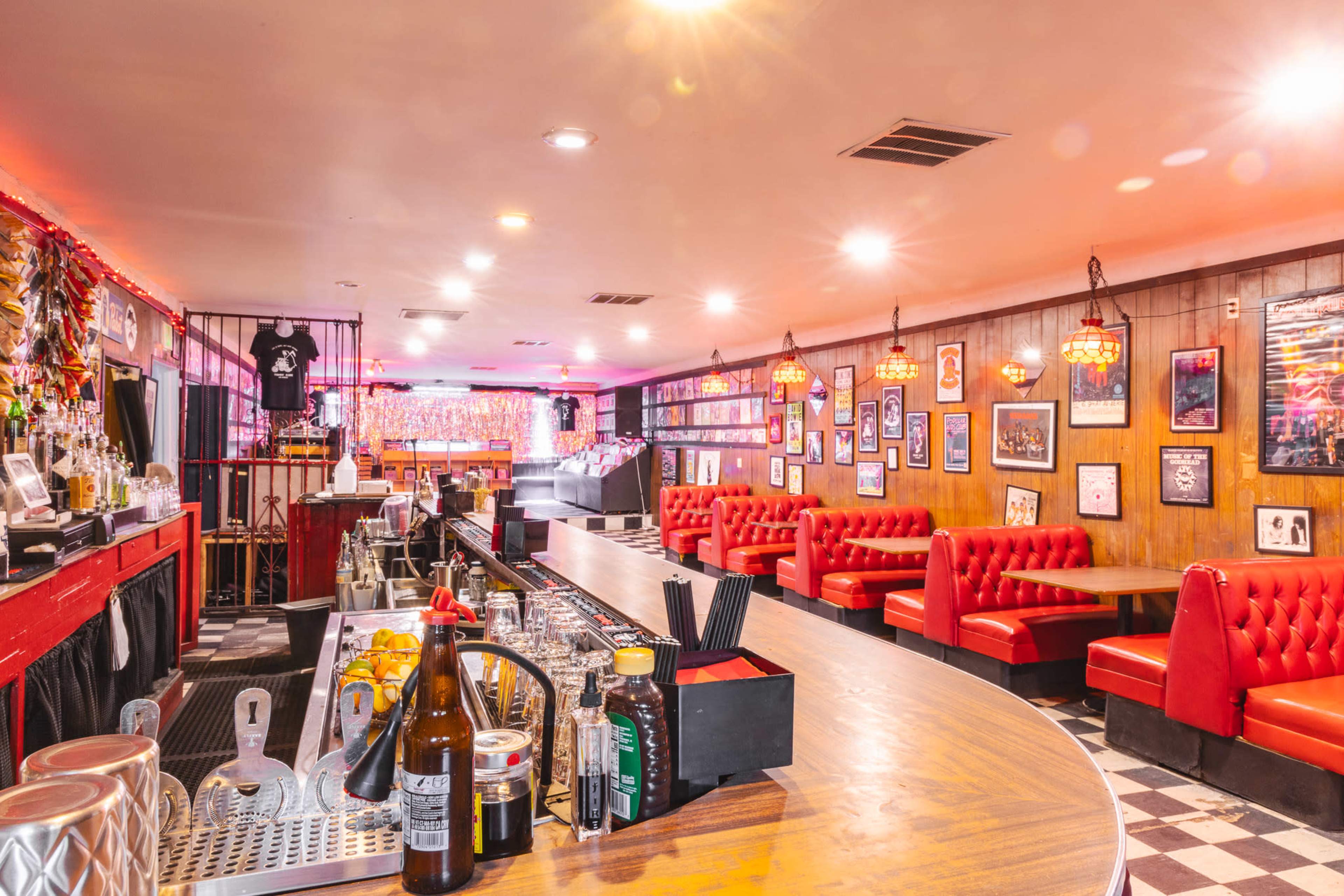 The image shows a bar area with a curved counter, red upholstered seating, and decorated walls featuring framed artwork.