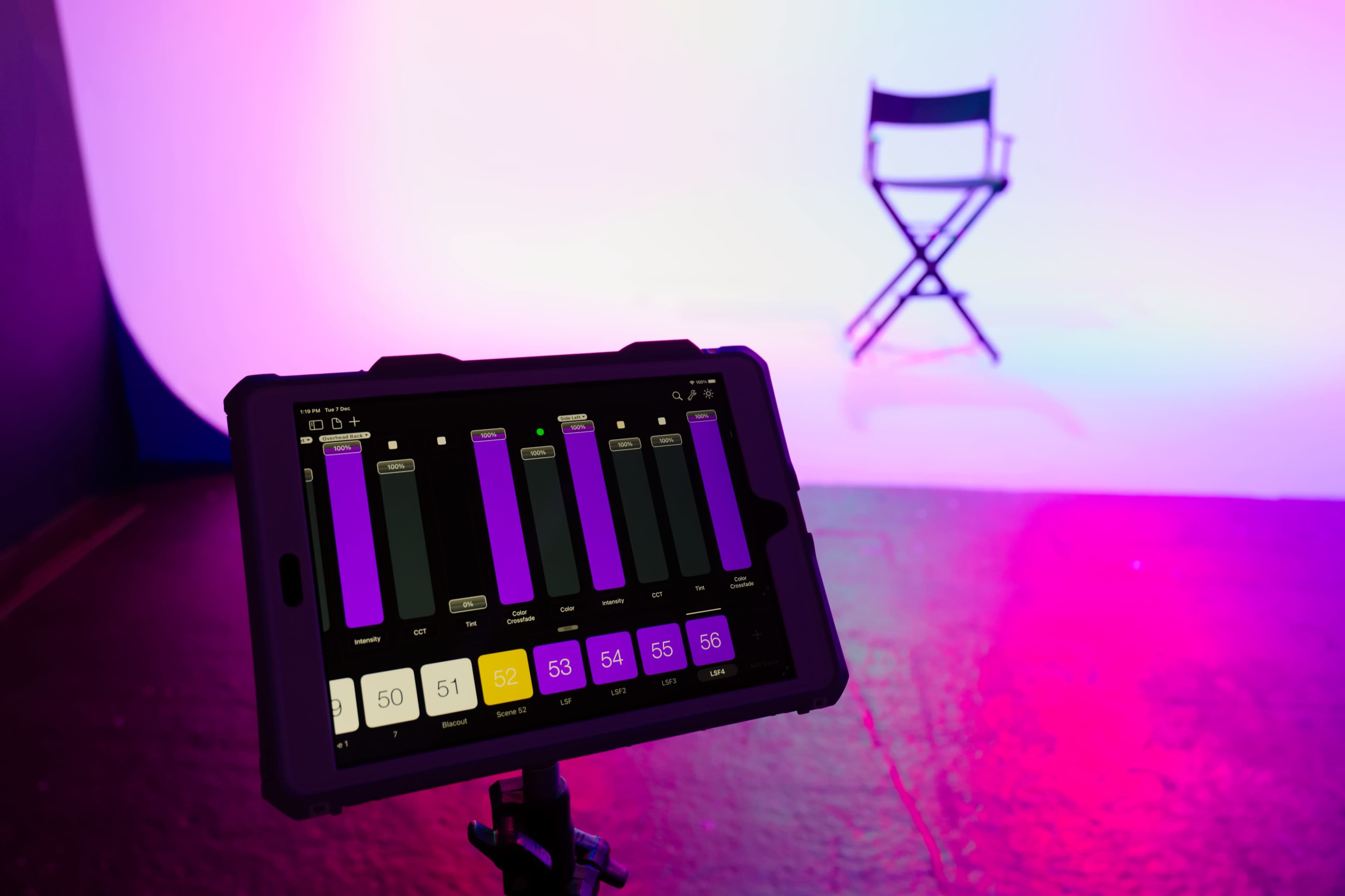 A tablet displaying various color settings is positioned in front of an empty director's chair against a gradient purple backdrop.