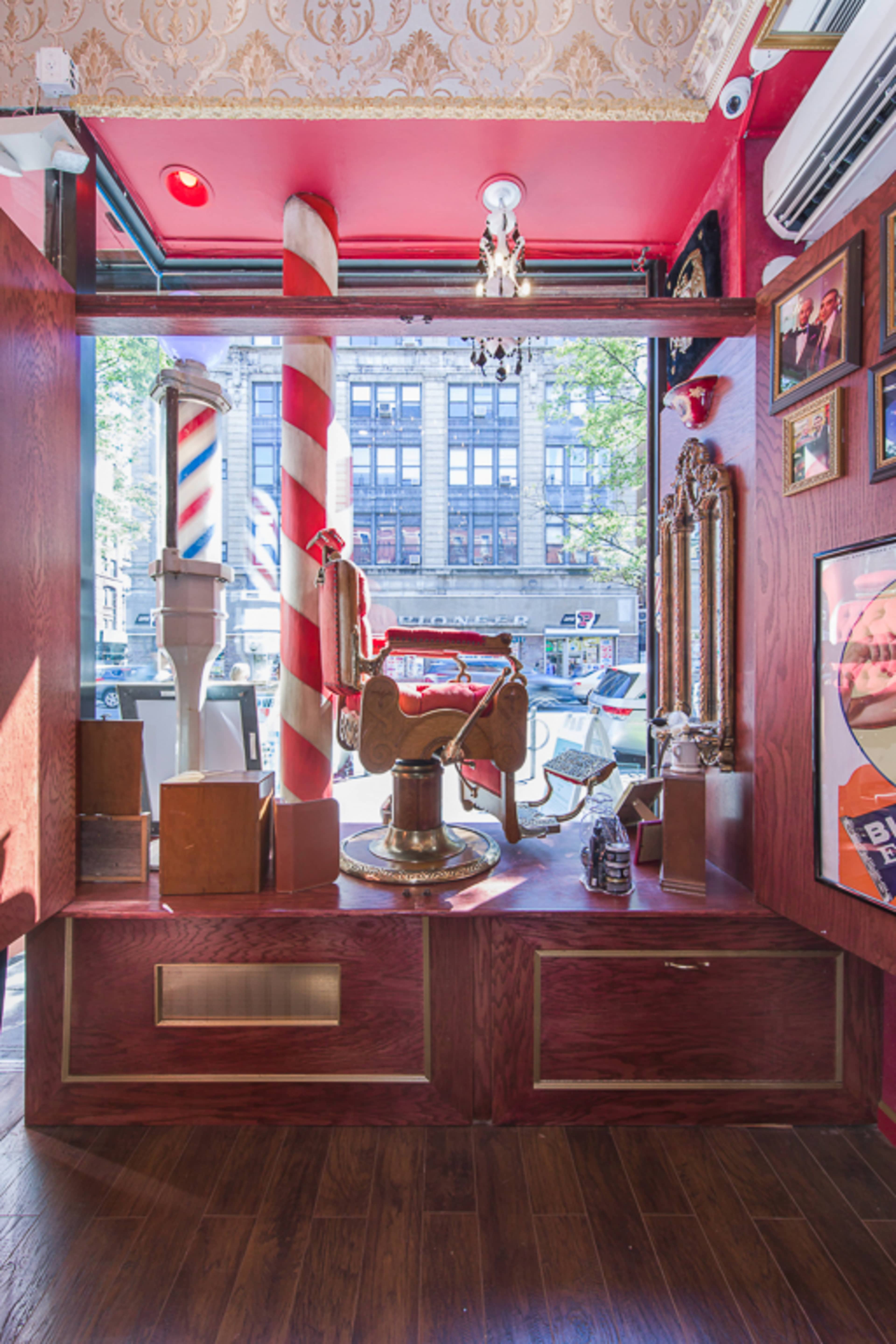 The interior of a barber shop featuring a vintage barber chair, striped poles, ornate decor, and framed photographs on the walls.