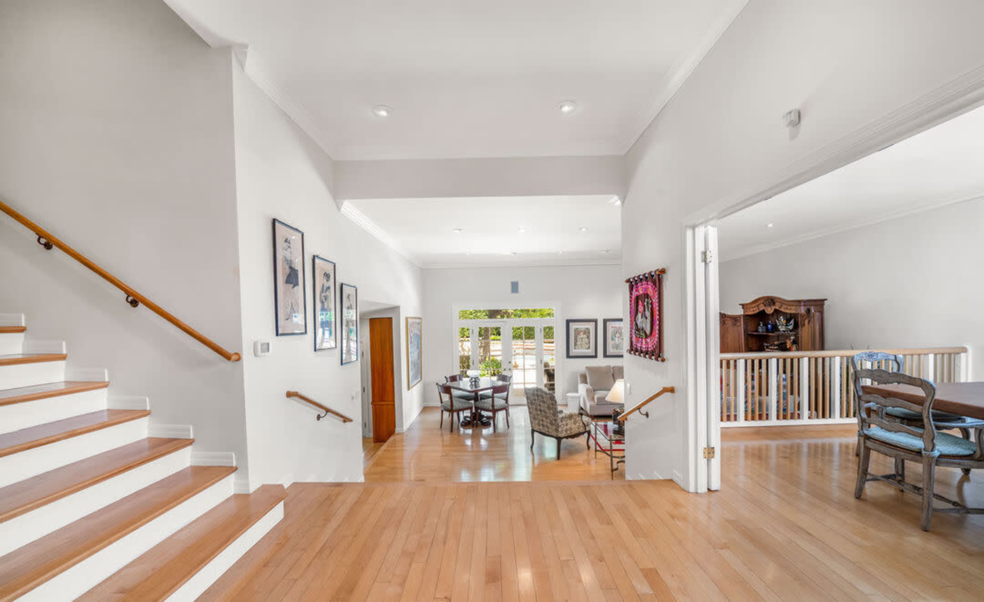 The image shows a spacious entryway with wooden stairs on one side and an open living and dining area visible in the background.