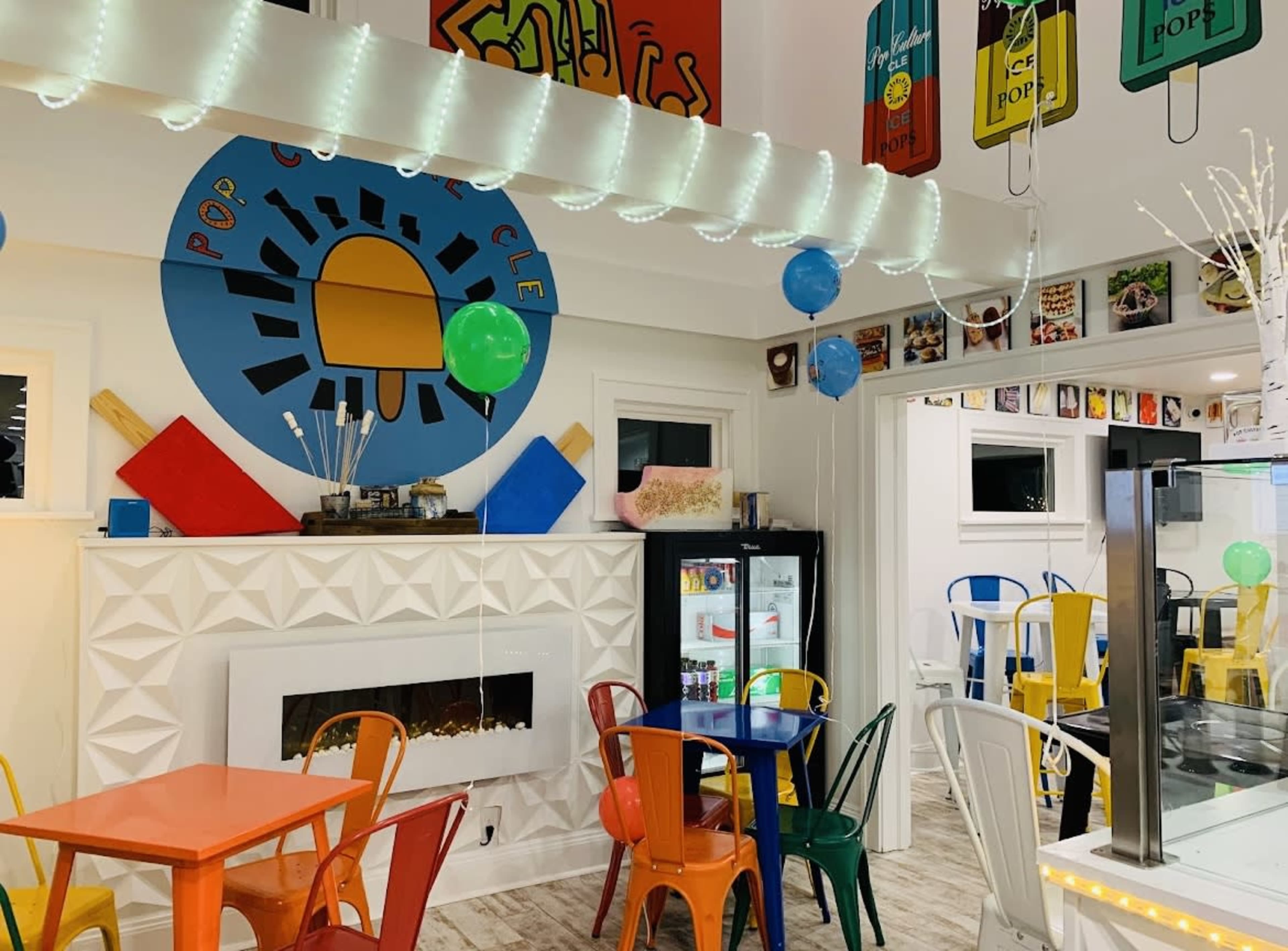 A colorful cafe interior with a decorative wall mural, assorted chairs around tables, and shelves displaying various items.
